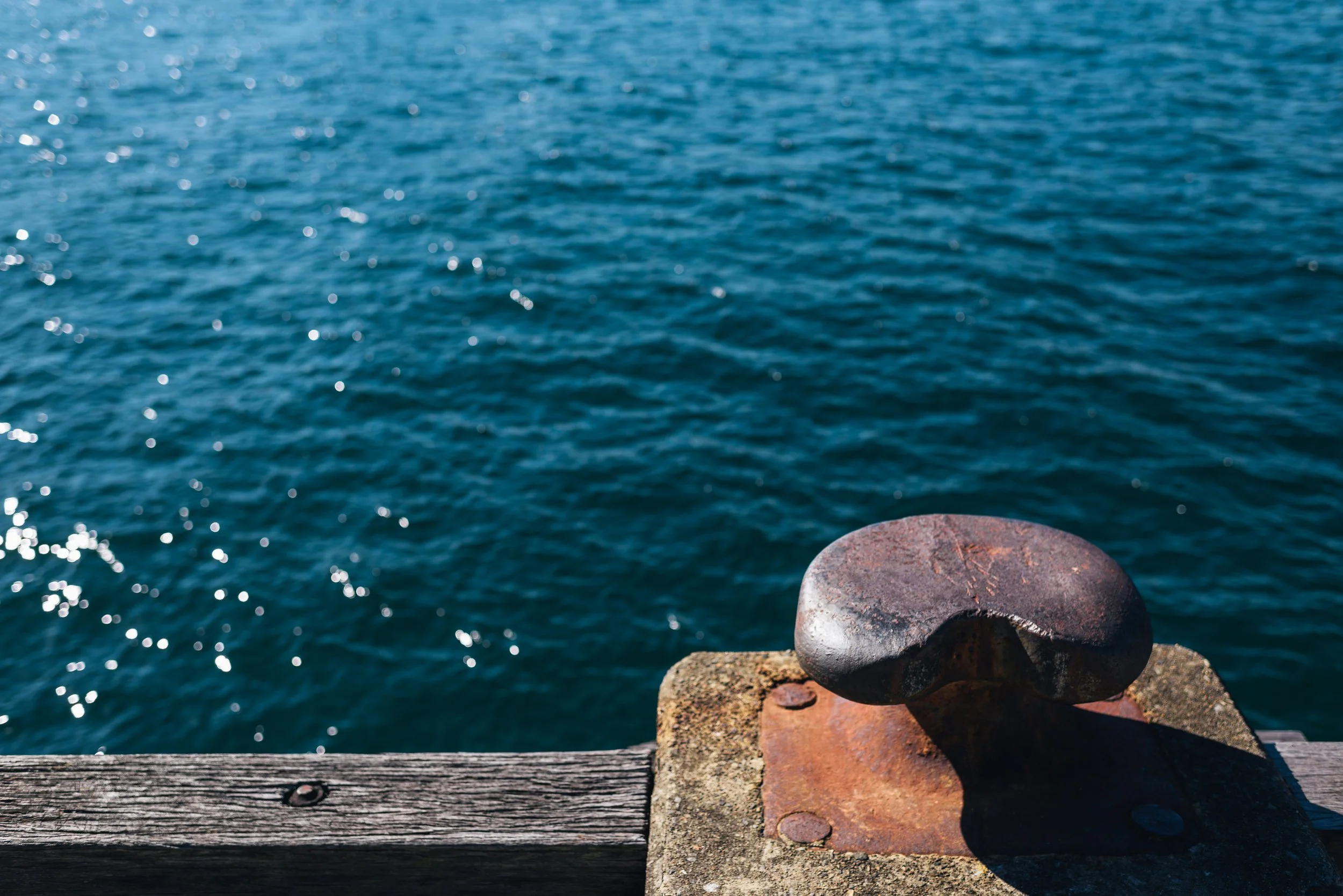 Close-up view of stacked rocks on a wooden plank near a blue body of water during daytime.