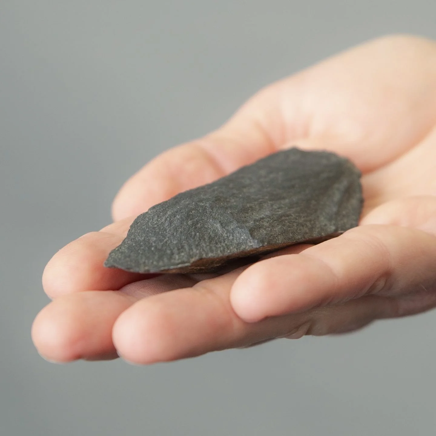 Hand holding a dark, pointed, rough-textured stone.