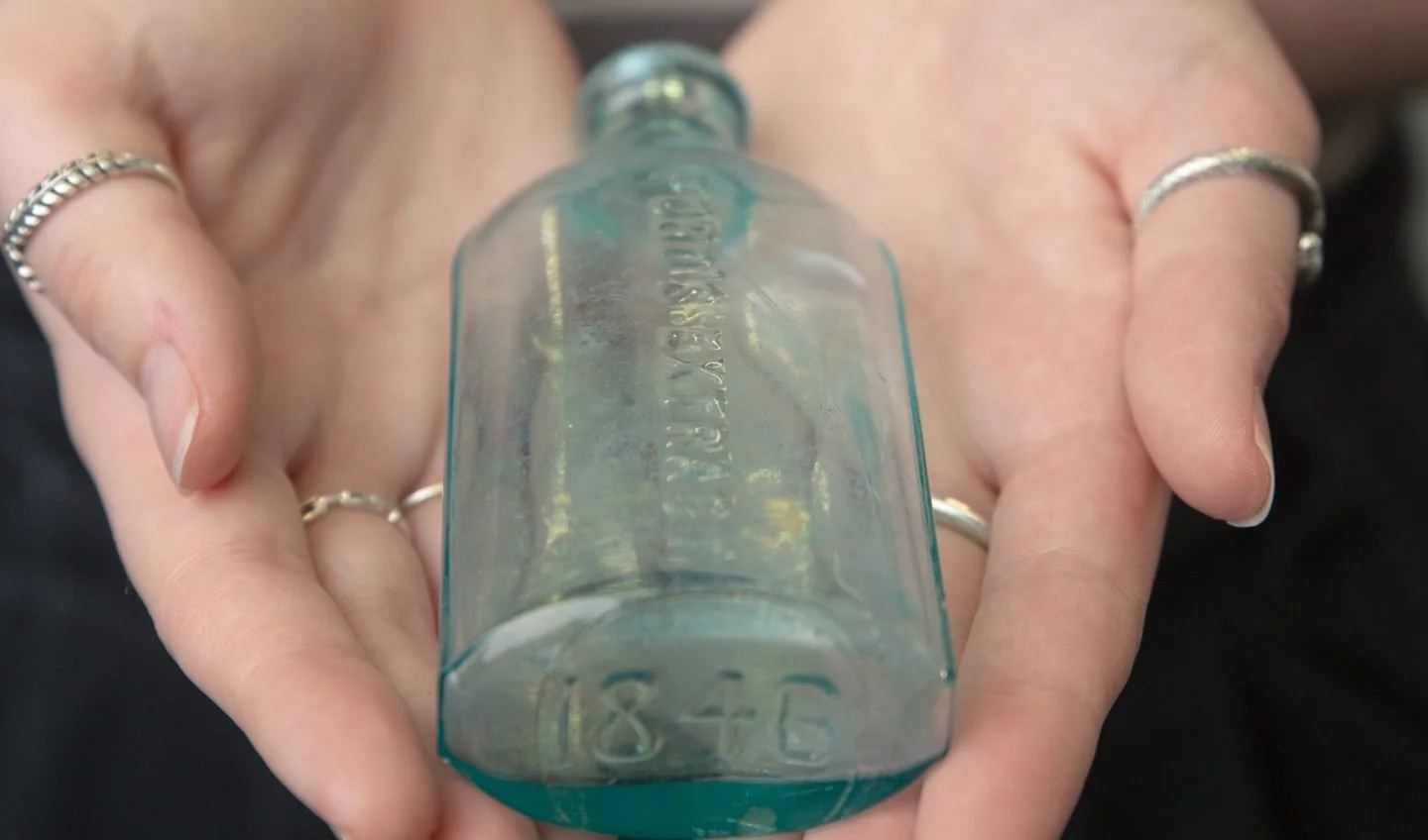 Person holding a small vintage glass bottle with embossed numbers and text.