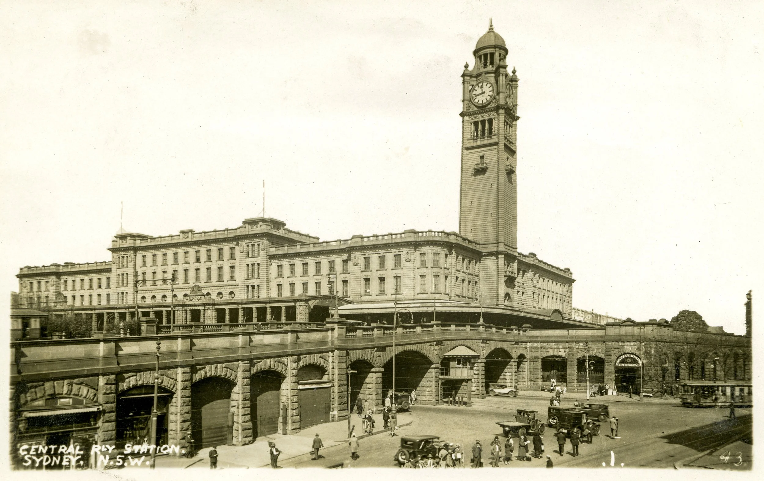 Old black and white photograph of Central Railway Station in Sydney, showing a tall clock tower, historic building, and street scene with vintage cars and pedestrians.