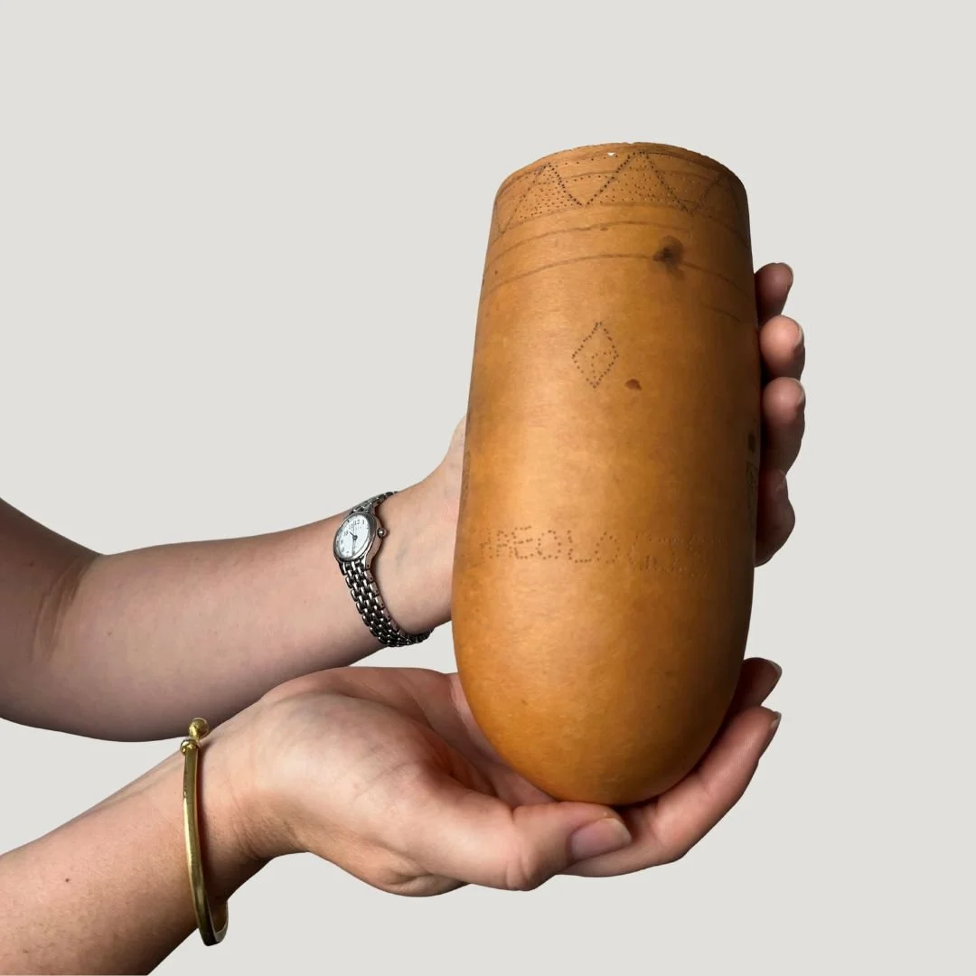Two hands holding a large gourd with engraved designs and text.