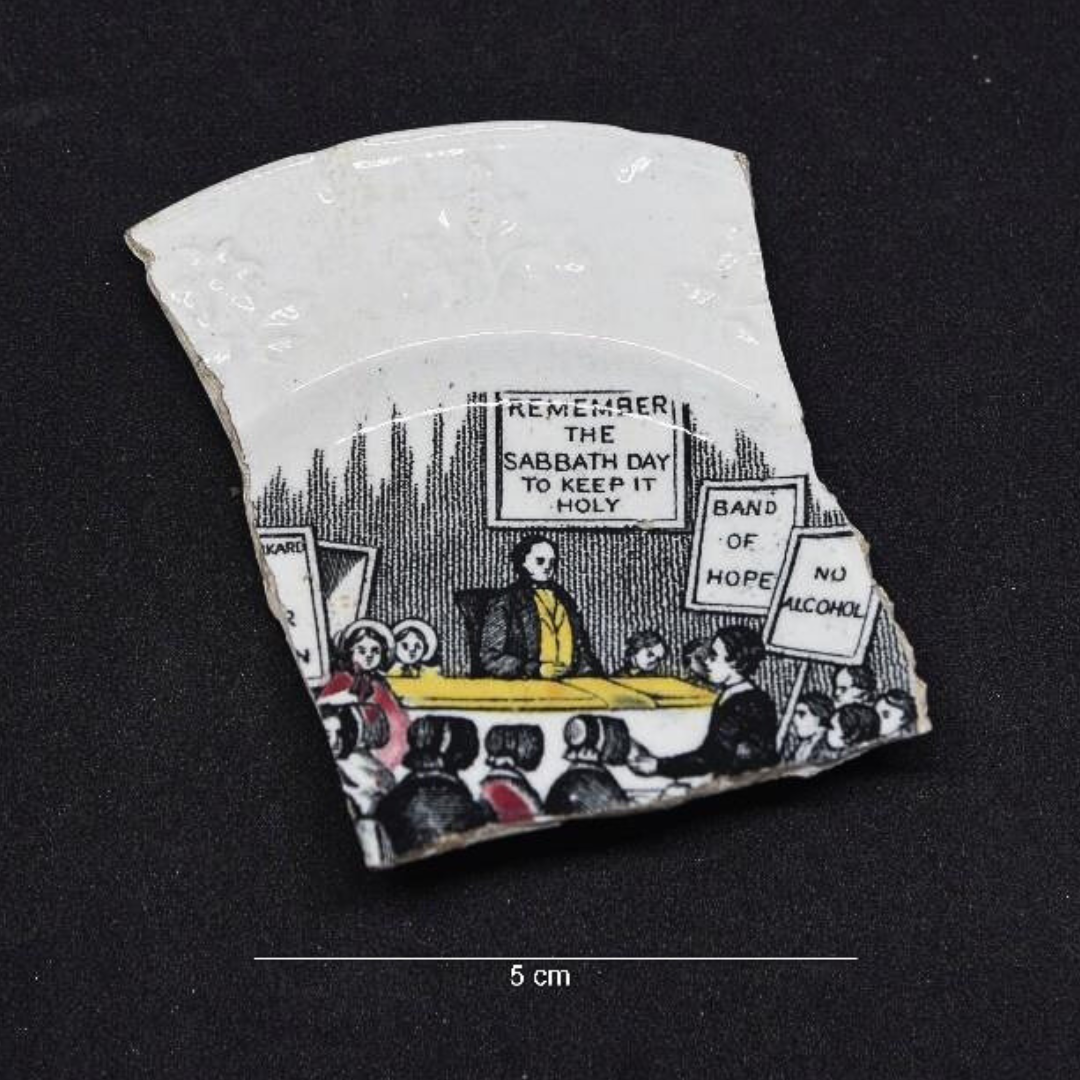 A small piece of broken ceramic with a drawing depicting a meeting or gathering, with signs that read 'Remember the Sabbath Day to Keep It Holy', 'Band of Hope', and 'No Alcohol.'