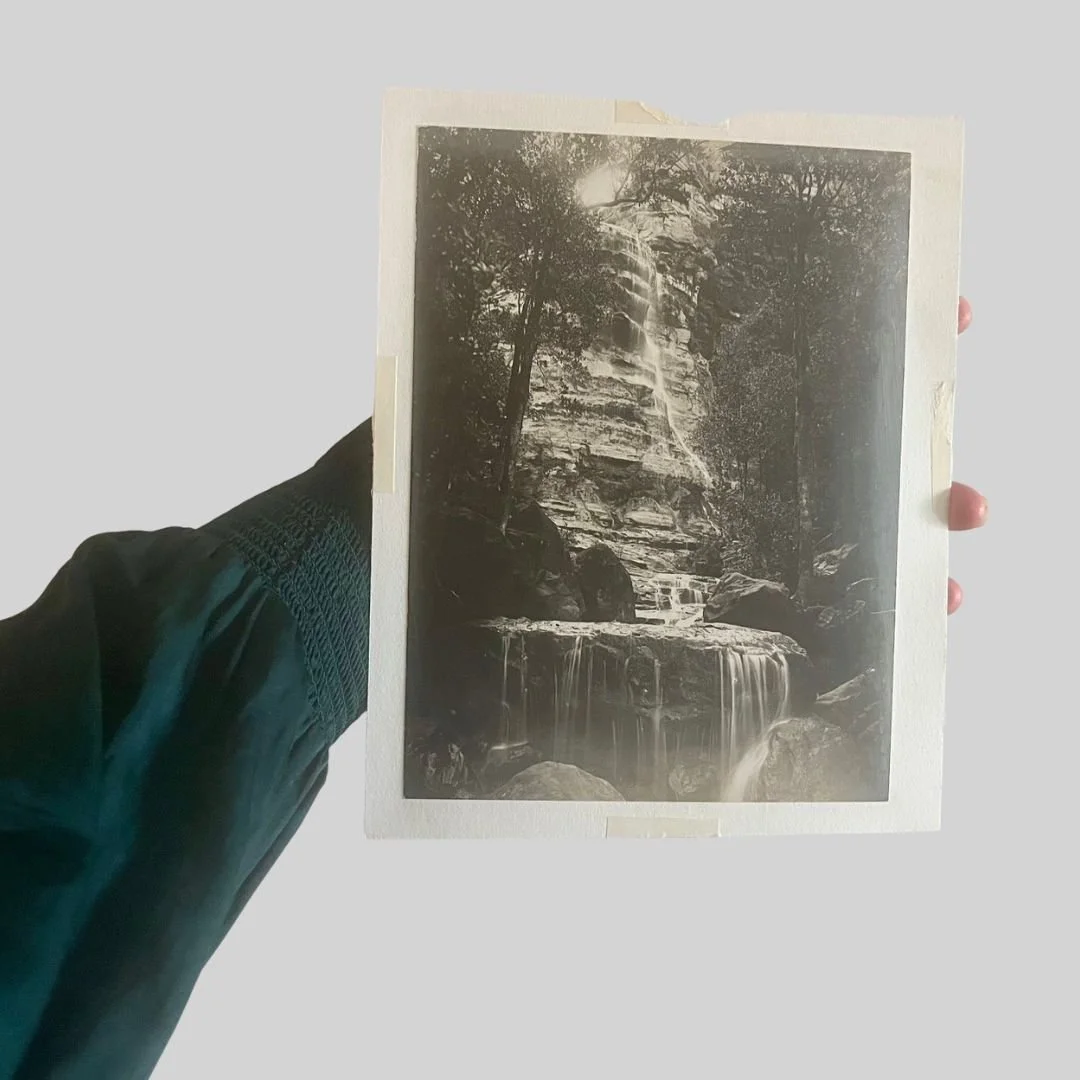 Black and white photo of a waterfall flowing over rocks surrounded by trees.
