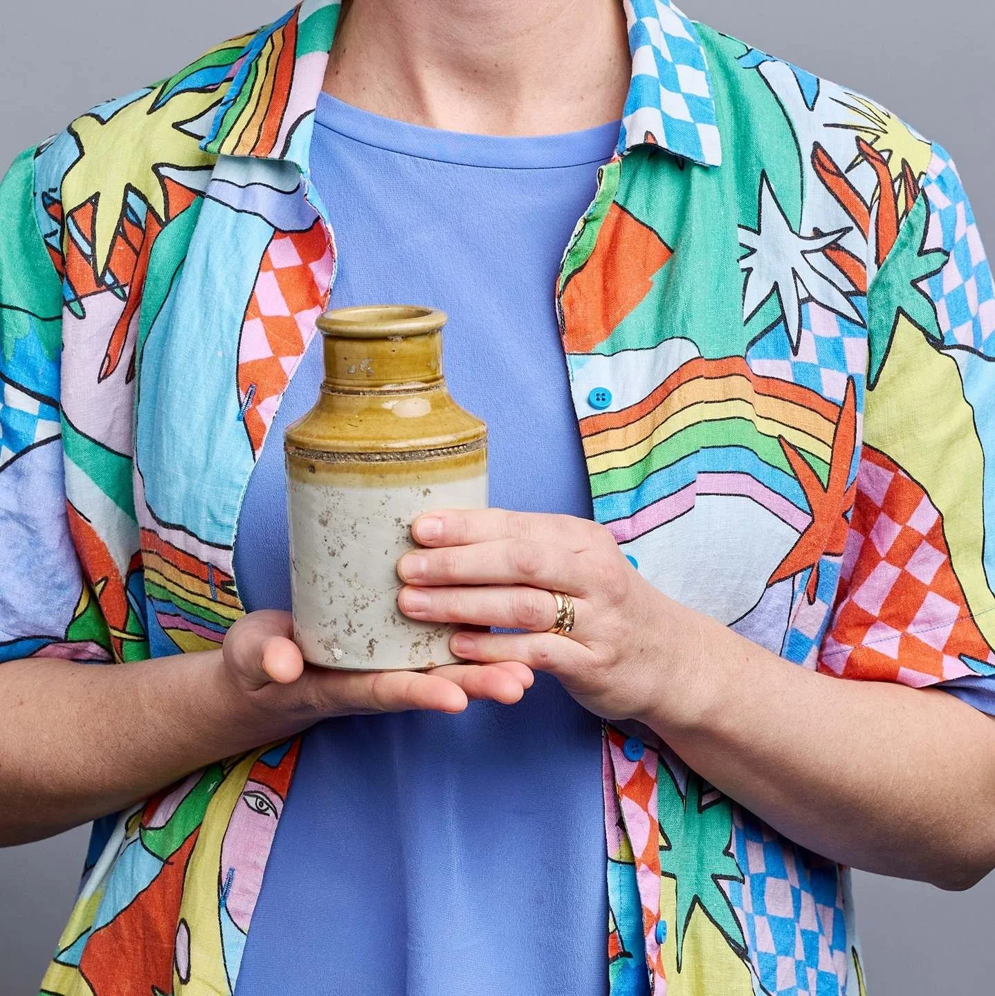Person wearing a colorful, patterned shirt and holding a ceramic jar with both hands.
