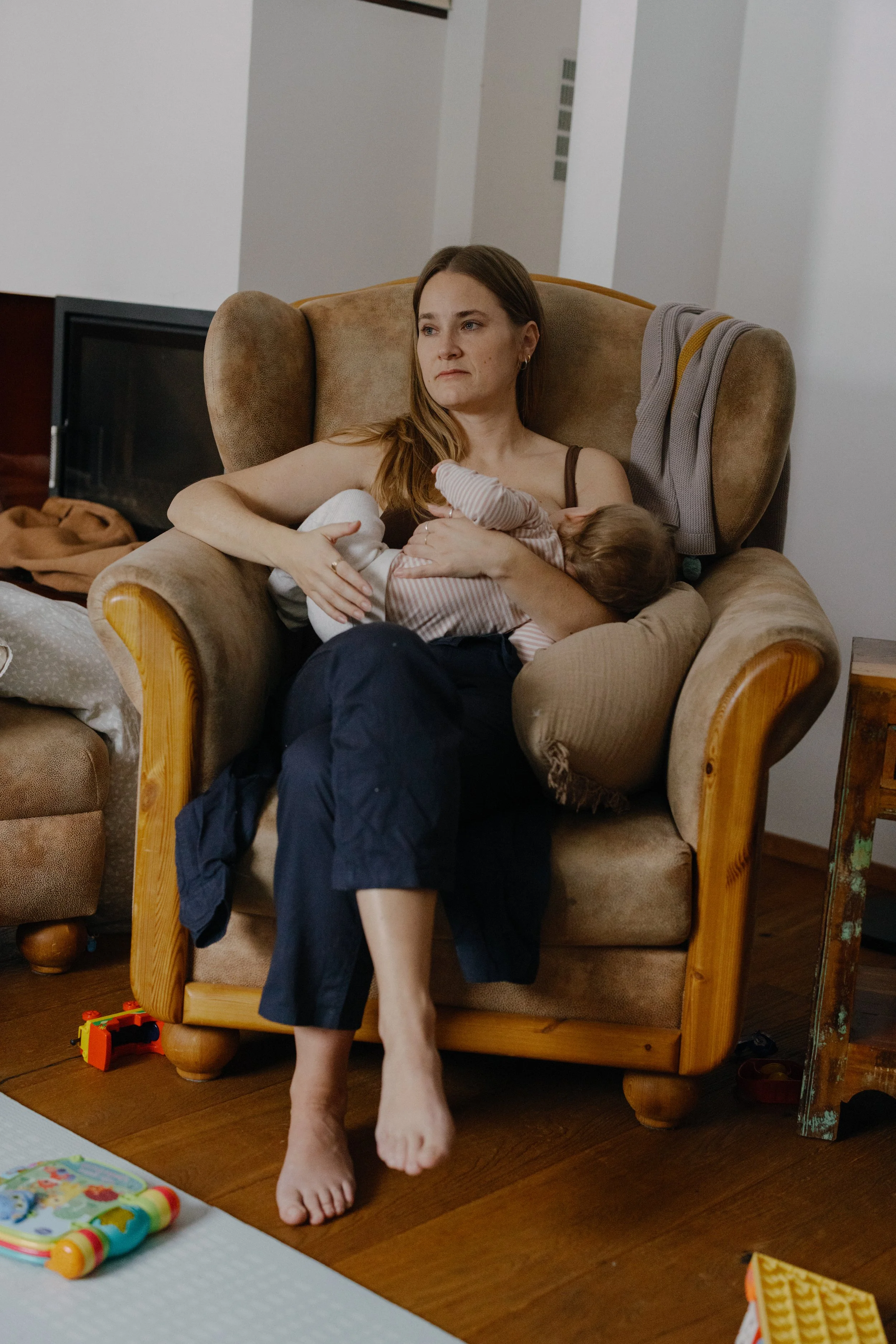 A woman sitting in a cozy armchair, breastfeeding a baby.