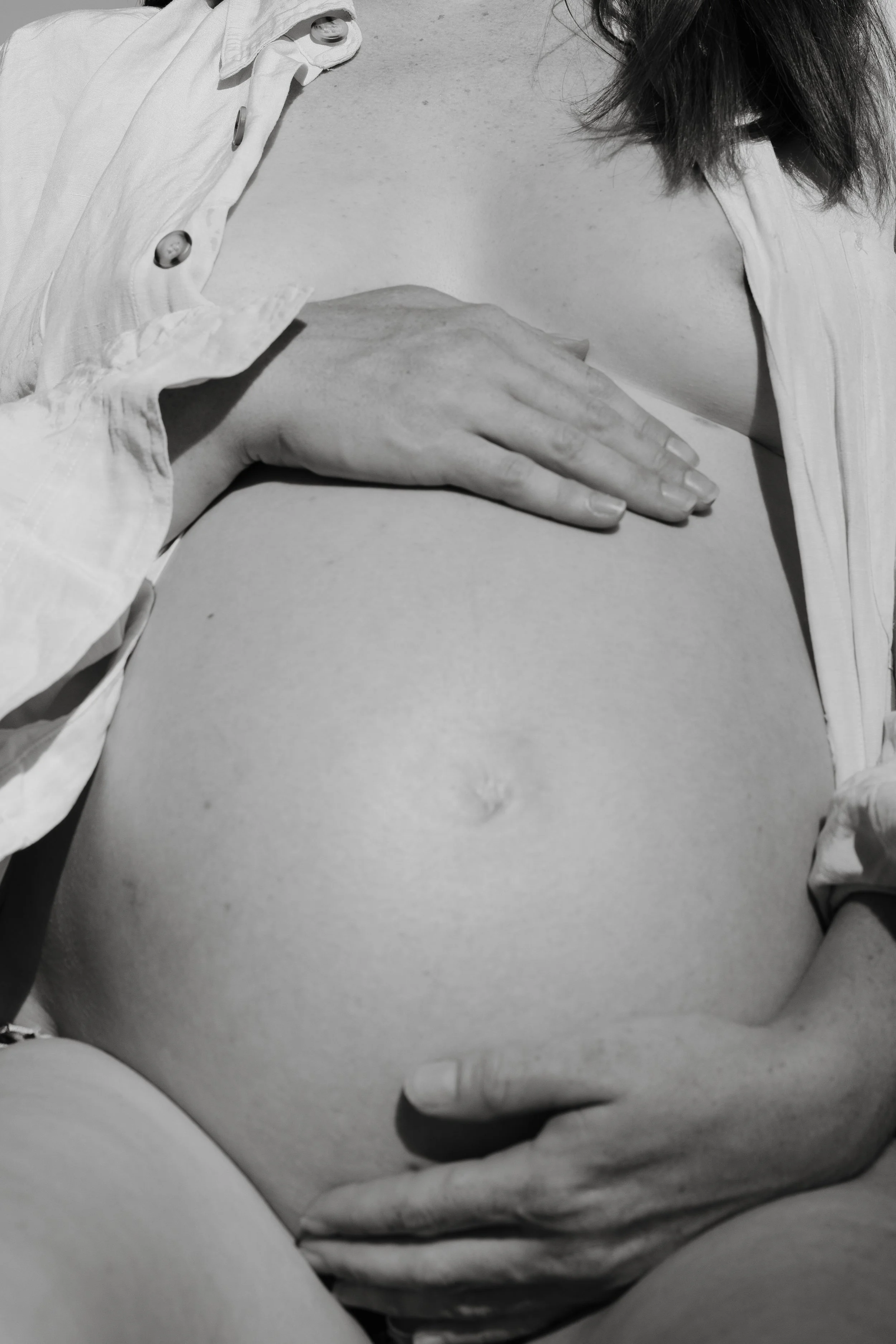 Close-up of a person's exposed stomach with two hands resting on it, one hand above and one hand below, wearing an open button-up shirt.