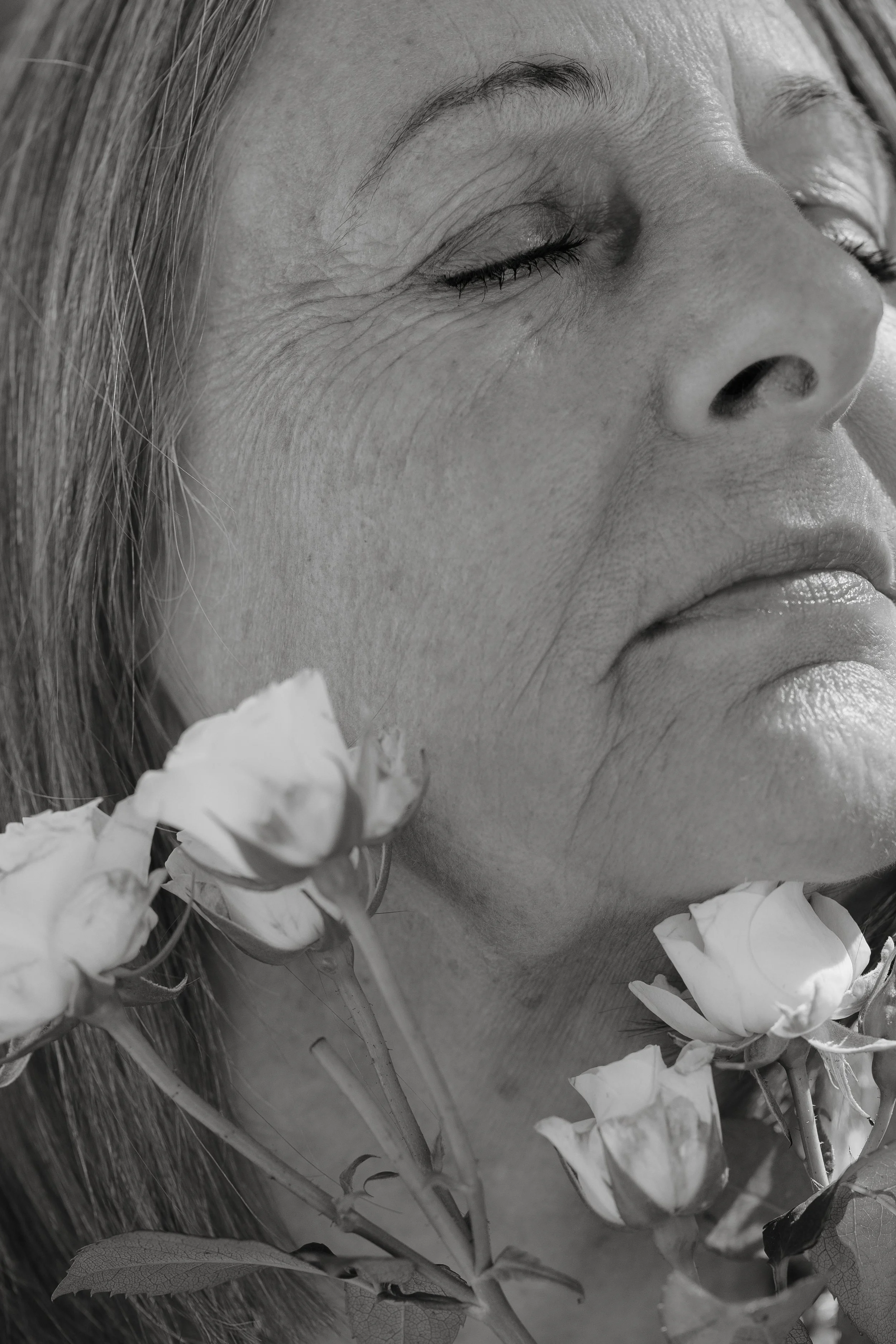 Close-up of a middle-aged woman's face in black and white, with closed eyes and a calm expression, surrounded by flowers.