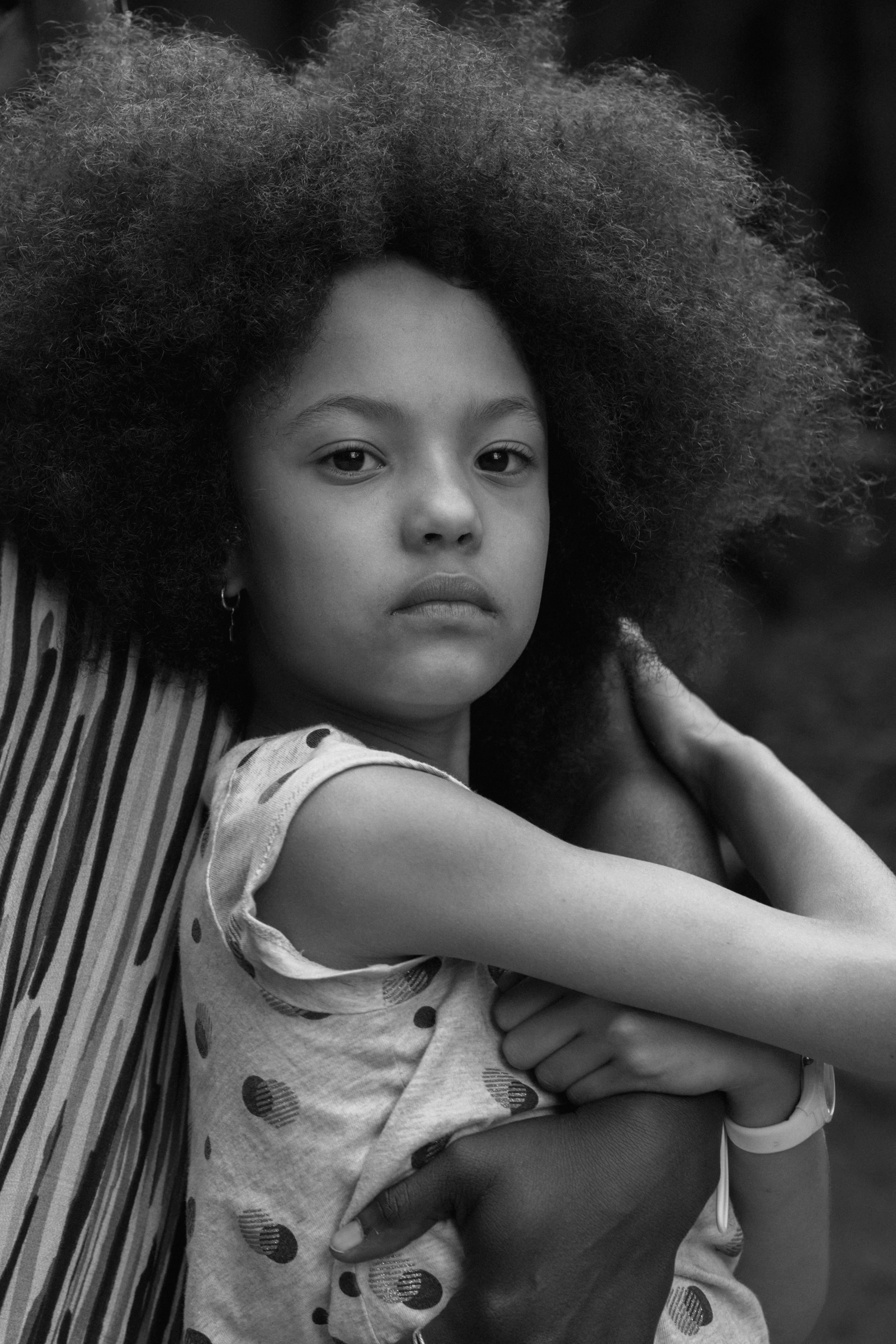 A black and white portrait of a young girl with curly hair, wearing a polka-dot shirt, being carefully held by someone.