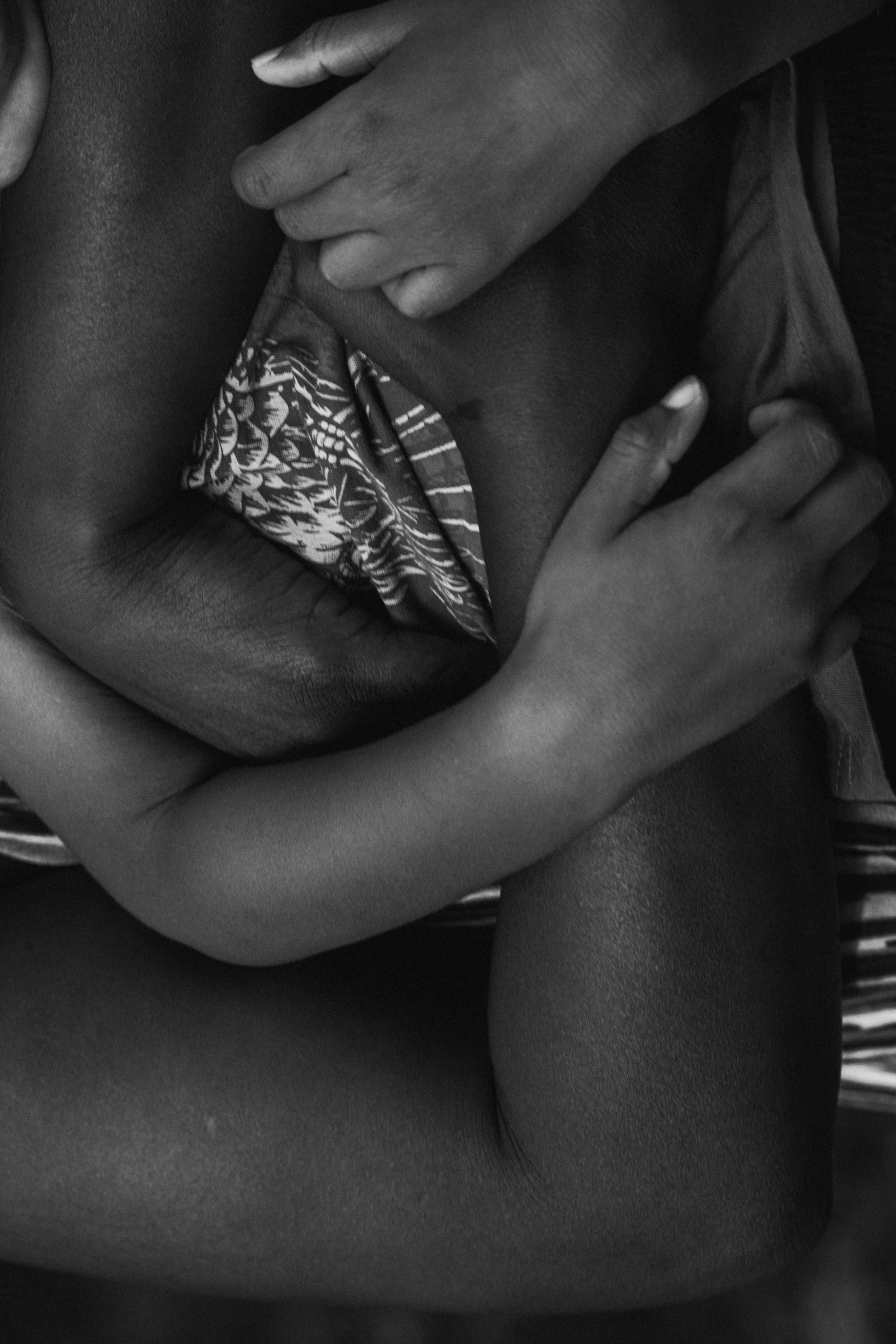 Close-up of a person holding a smaller person's upper body, with both arms wrapped around the smaller person in a comforting embrace, in black and white.