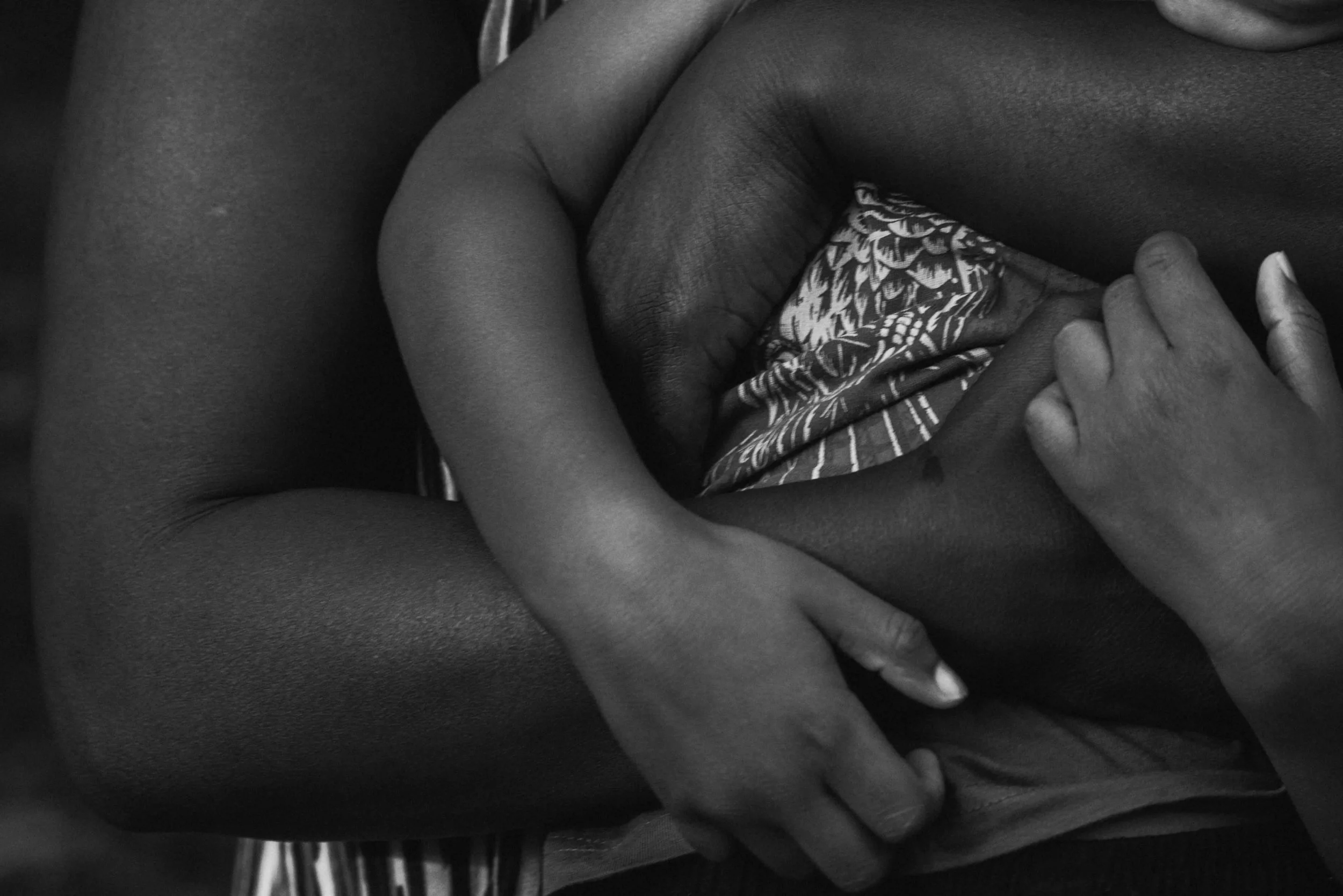 Close-up of a person holding a smaller person's upper body, with both arms wrapped around the smaller person in a comforting embrace, in black and white.