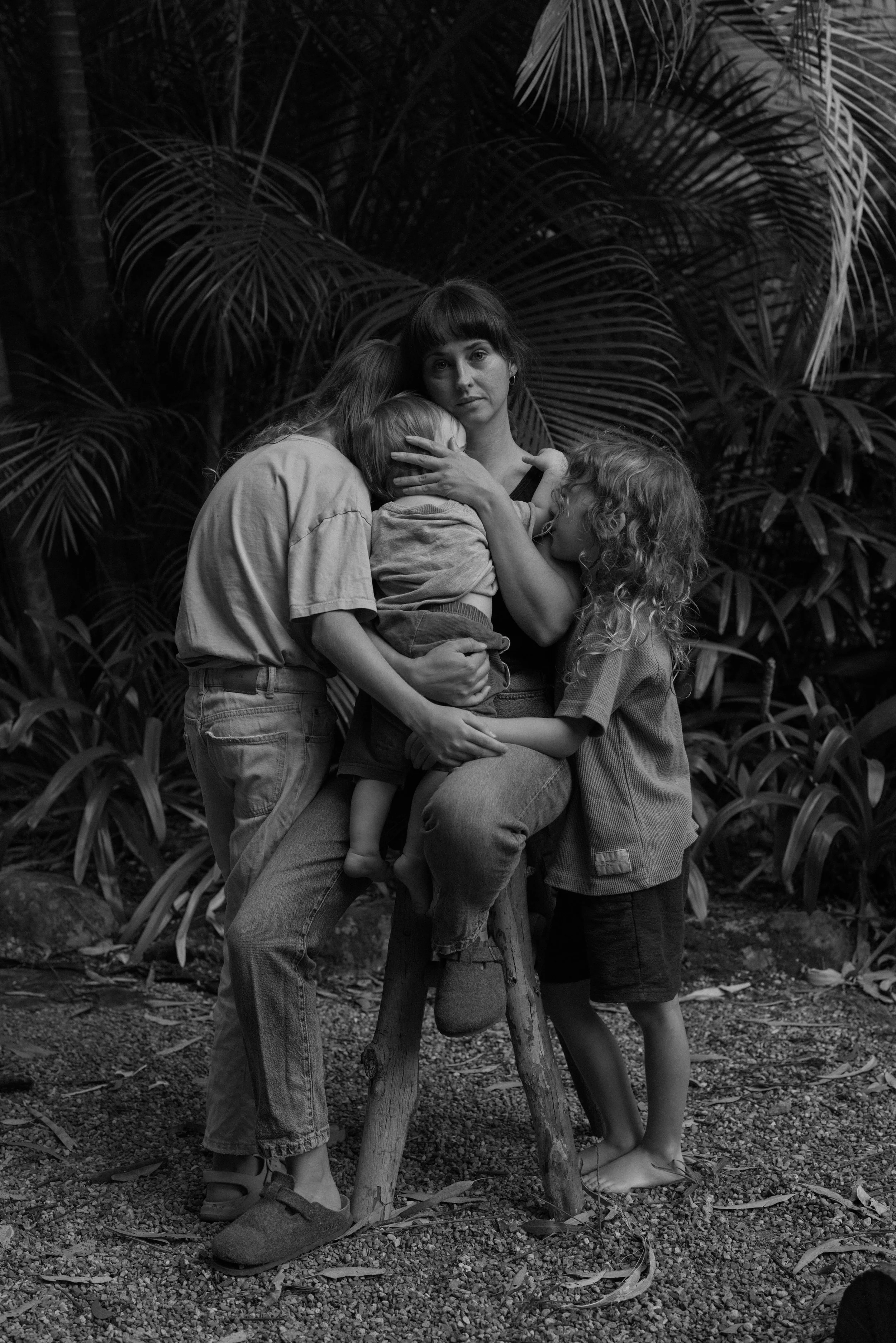 A woman with three children in a jungle setting, embracing and comforting each other. The scene is in black and white.
