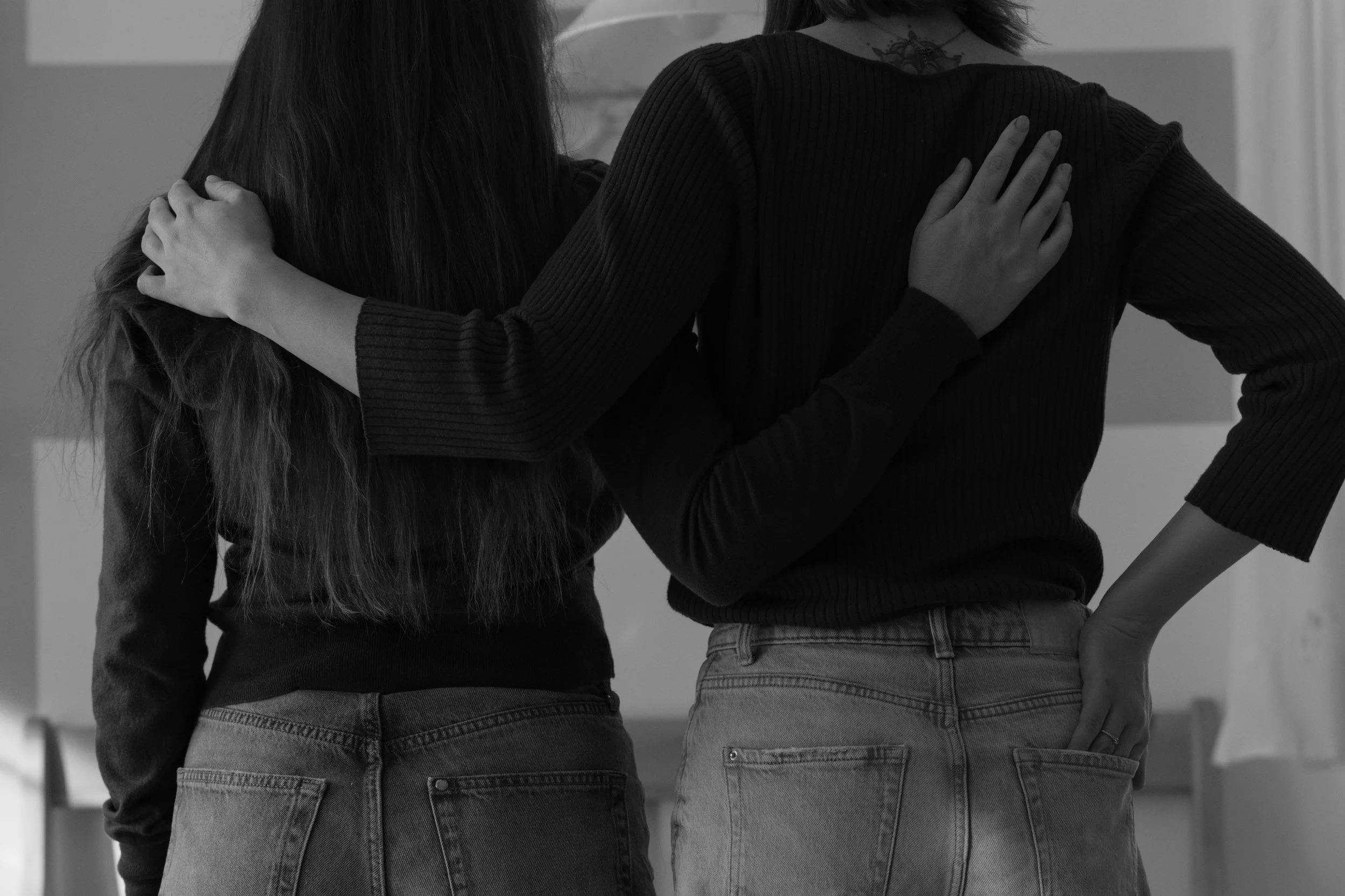 Two women standing close together, with their arms around each other's shoulders, in a supportive embrace.