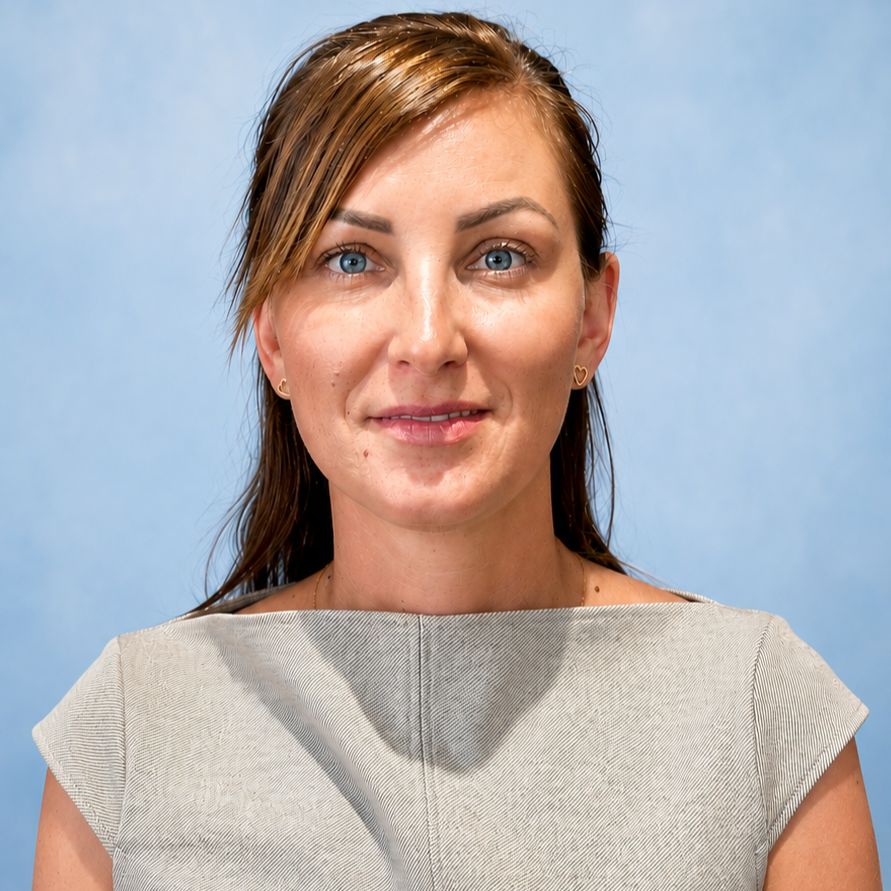 A woman with brown hair, blue eyes, and light skin, wearing a light beige top and small heart-shaped earrings, standing against a light blue background.