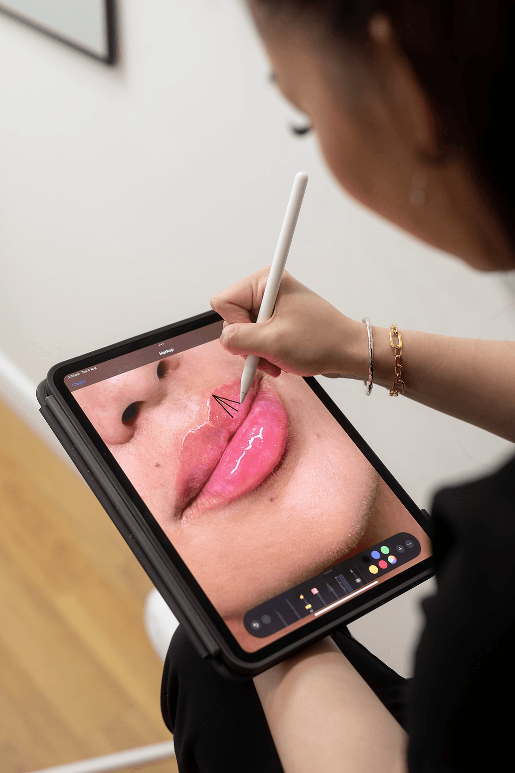 A woman using a stylus on a tablet to edit a close-up photo of lips with annotations.