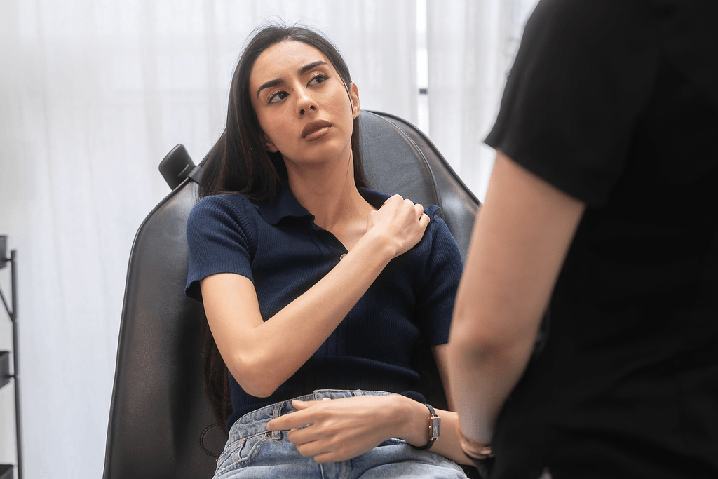 A woman with long dark hair sitting in a chair, looking concerned, speaking with nurse about shoulder pain