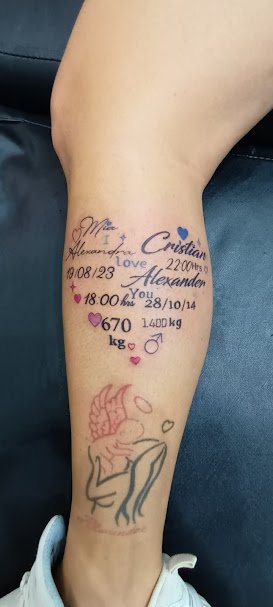 Tattoo on a person's lower leg featuring various elements including a small purple heart with a crown, a drawing of a fairy with wings, and several words, dates, and numbers such as "Alexandrina love", "2200hrs", "28/10/14", and "670 kg".