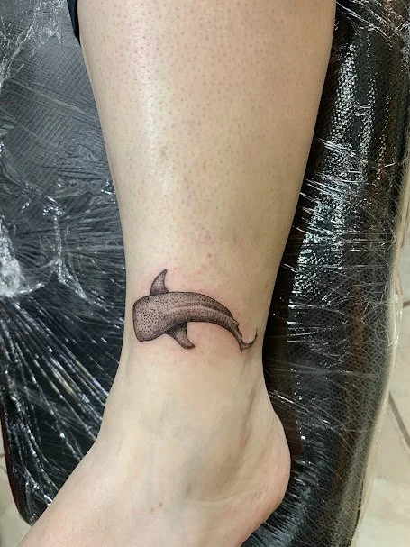 A tattoo of a cartoon-style dolphin on a person's ankle.