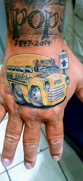 Tattoo of a yellow delivery truck on a person's hand, with text and a tablet device in the background.
