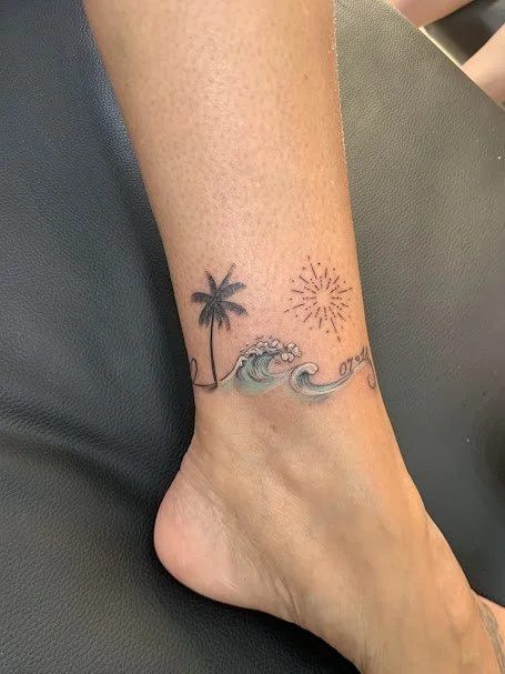 Tattoo of a palm tree, ocean waves, and a firework on ankle.