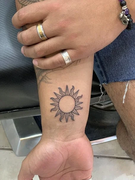 A person's wrist with a sun tattoo and several rings and bracelets.