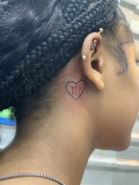Close-up of a woman's right side profile showing a small neck tattoo of a heart with the Virgo zodiac symbol inside it.