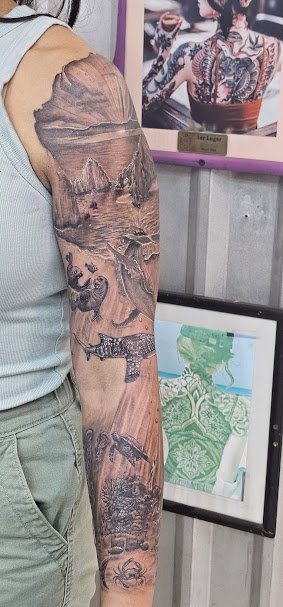 Tattoo of a scenic landscape with mountains, lakes, and wild animals on a person's arm.