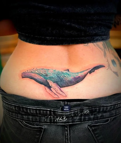 Tattoo of a whale on person's lower back.