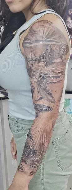 Close-up of a person's arm with a detailed black and gray landscape tattoo, including mountains, a river, and a waterfall.
