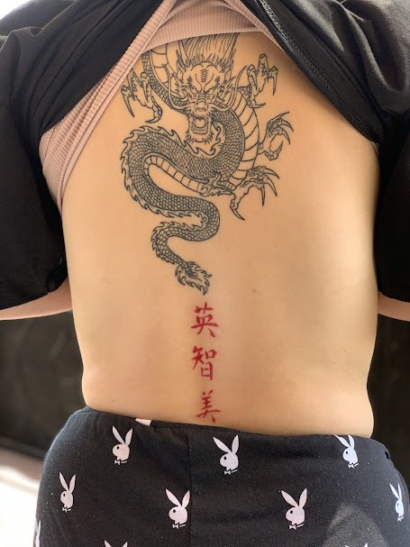 A tattoo of a dragon with a long, coiled body and claws on a person's lower chest, with three red Chinese characters below it.