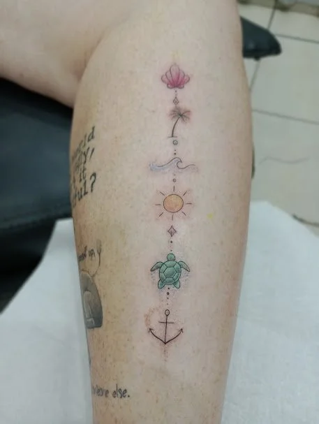 Colorful tattoo on person's arm featuring a flower, star, wave, sun, turtle, and anchor in vertical arrangement.