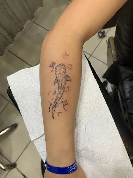 Tattoo of a whale with stars and geometric shapes on a person's forearm.