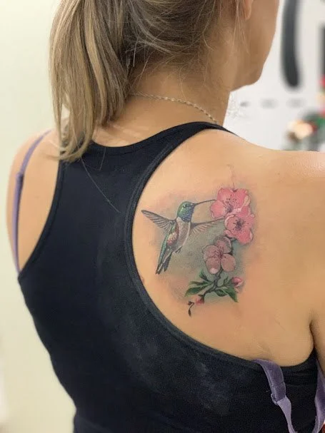 Tattoo of a hummingbird and pink flowers on a woman's shoulder