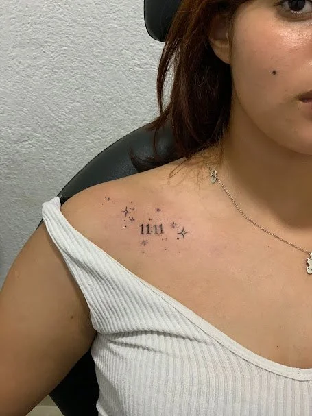 Tattoo of the time 11:11 and stars on the person's shoulder.