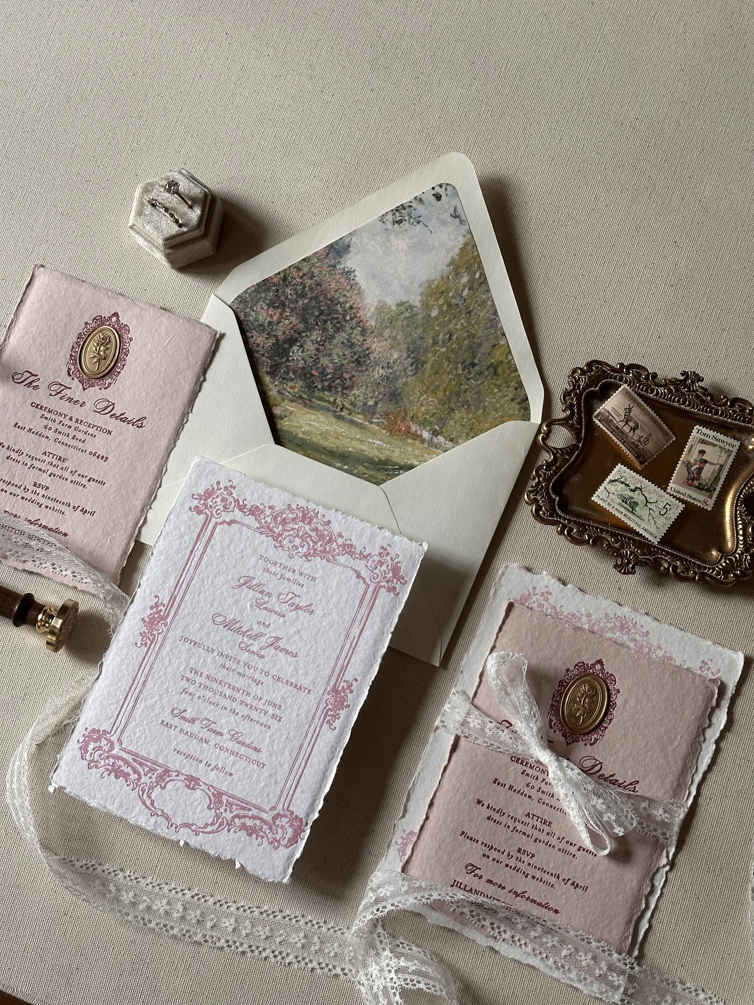 Wedding invitation with pink and white ornate details, a small decorative frame with vintage postage stamps, a floral scene inside an envelope, a lace ribbon, and a small fabric pouch on a beige surface.