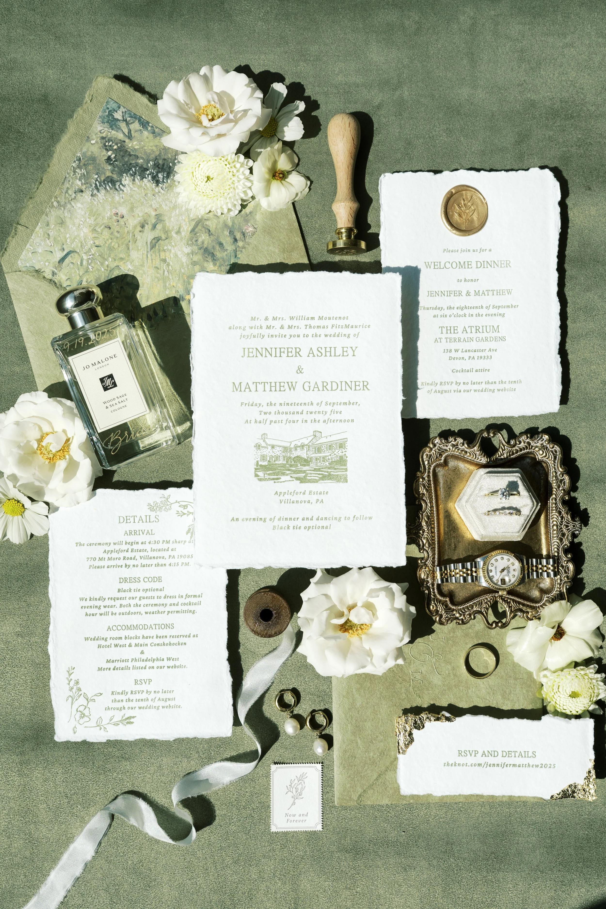 Wedding invitation, flowers, perfume, jewelry, ring, watch, and decorative items arranged on a surface.