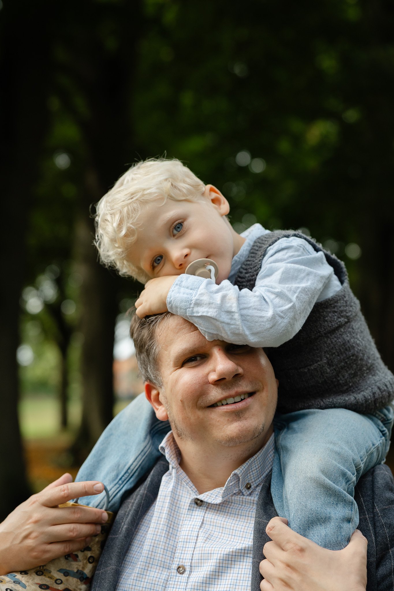 Lille 3-årig dreng har sut i munden og sidder på sine fars skuldre til udendørs familiefotografering i efteråret