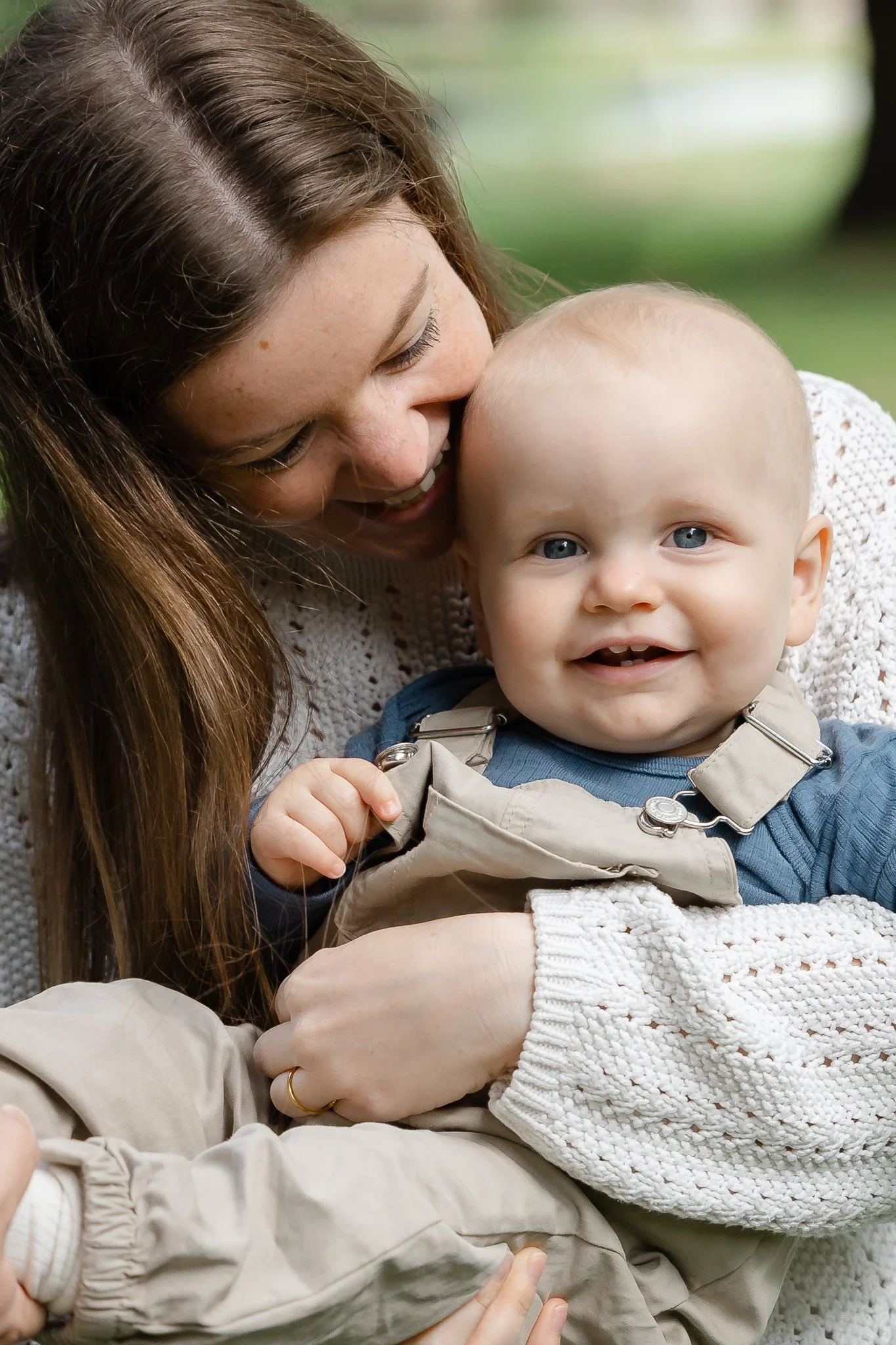 En kvinde holder en smilende baby i sine arme, de begge ser glade ud.