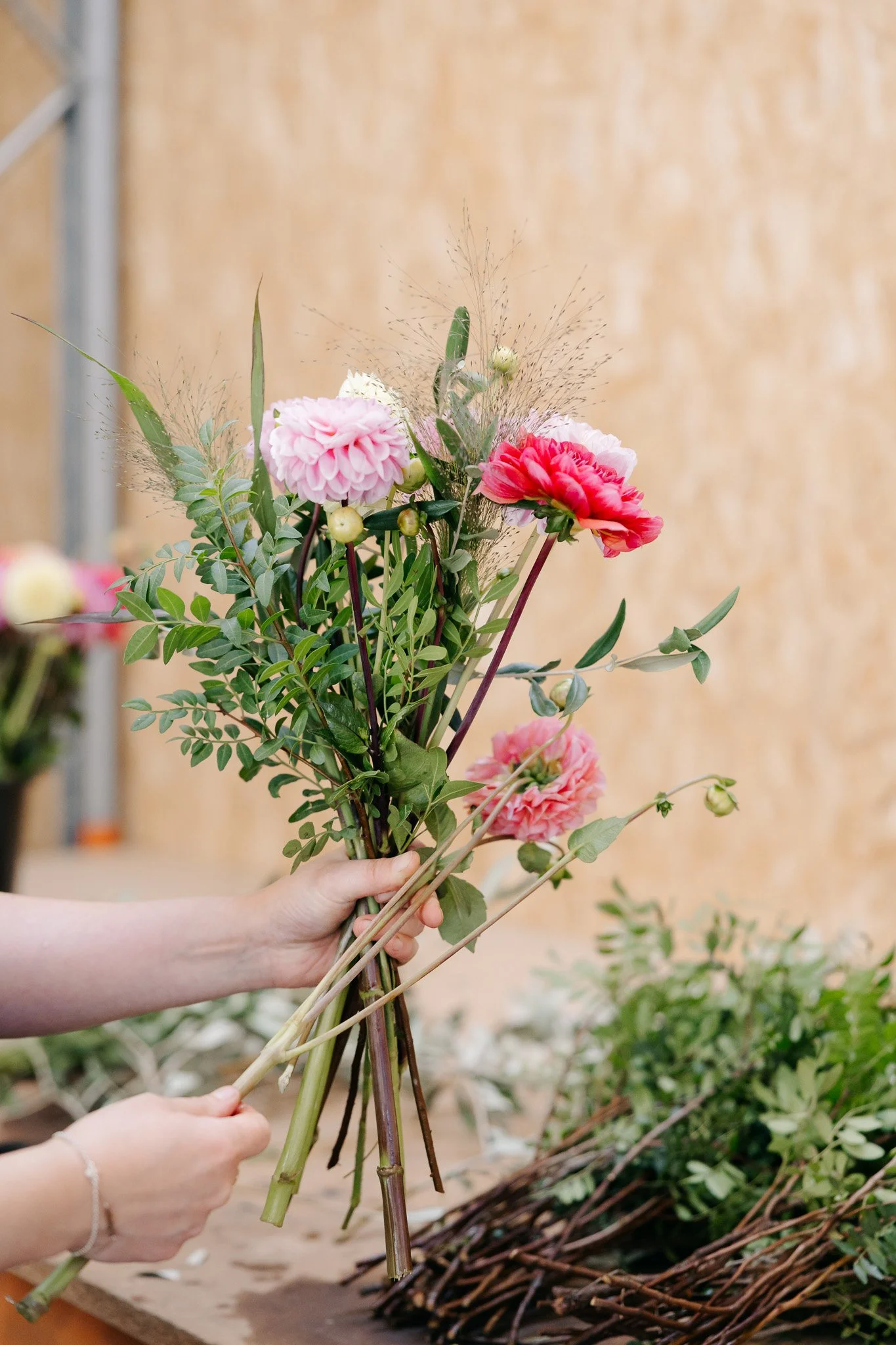 Hånd, der arrangerer en buket af lyserøde og hvide blomster med grønne blade.