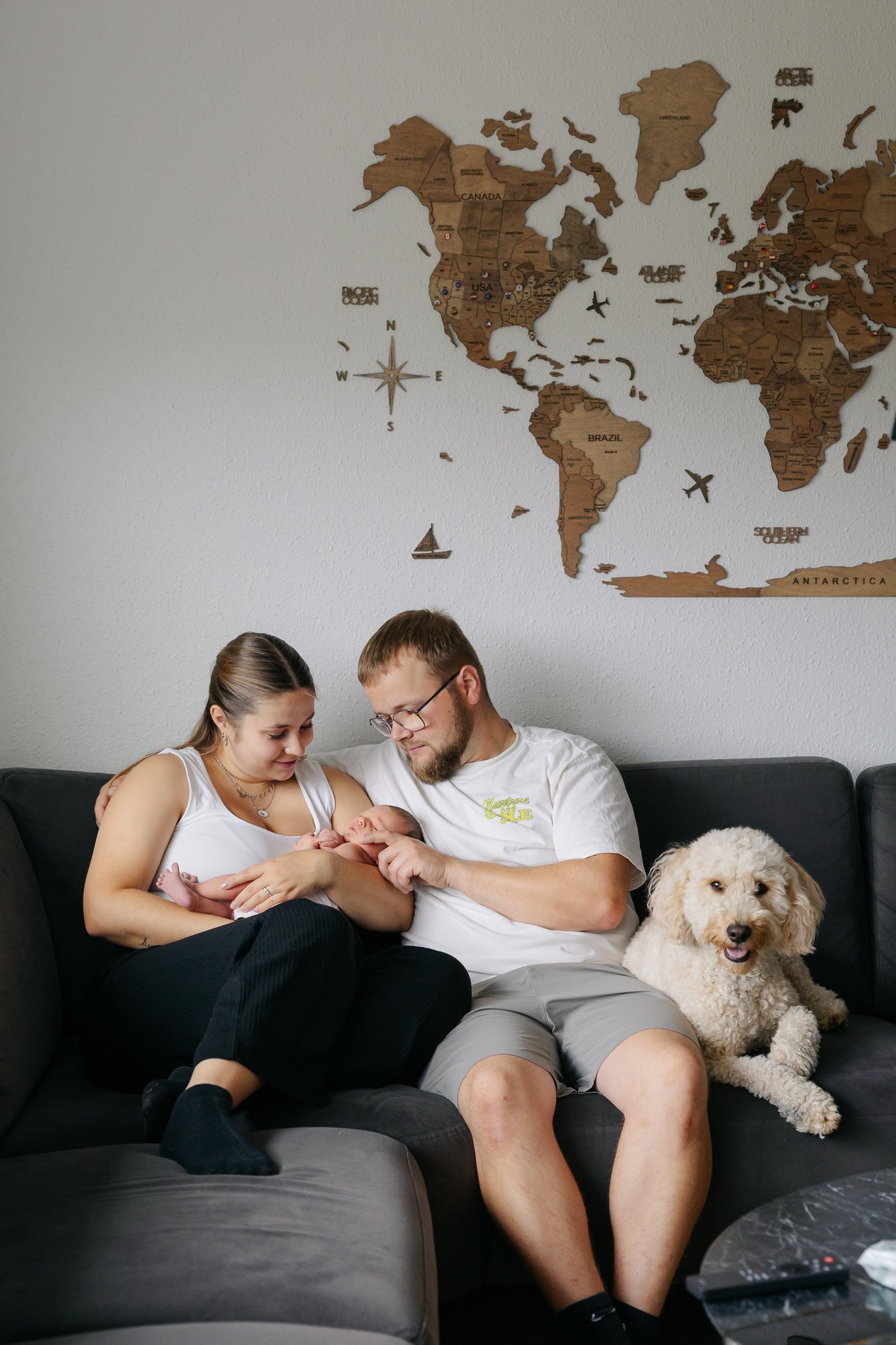 Nybagt familie sidder sammen i sofaen med deres nyfødte baby og hund.