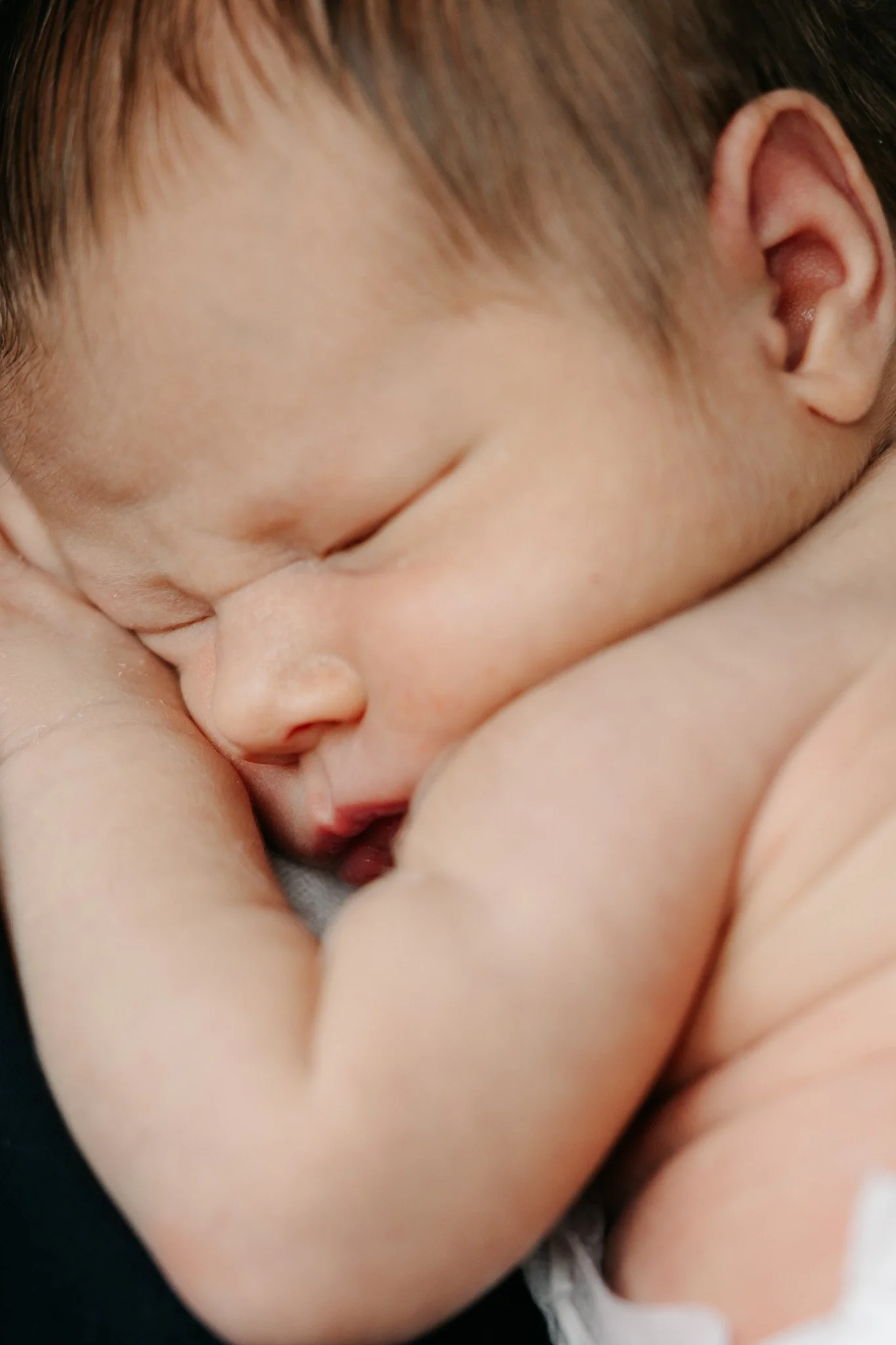 Nærbillede af nyfødt baby, der sover trygt med ansigtet hvilende mod armen.