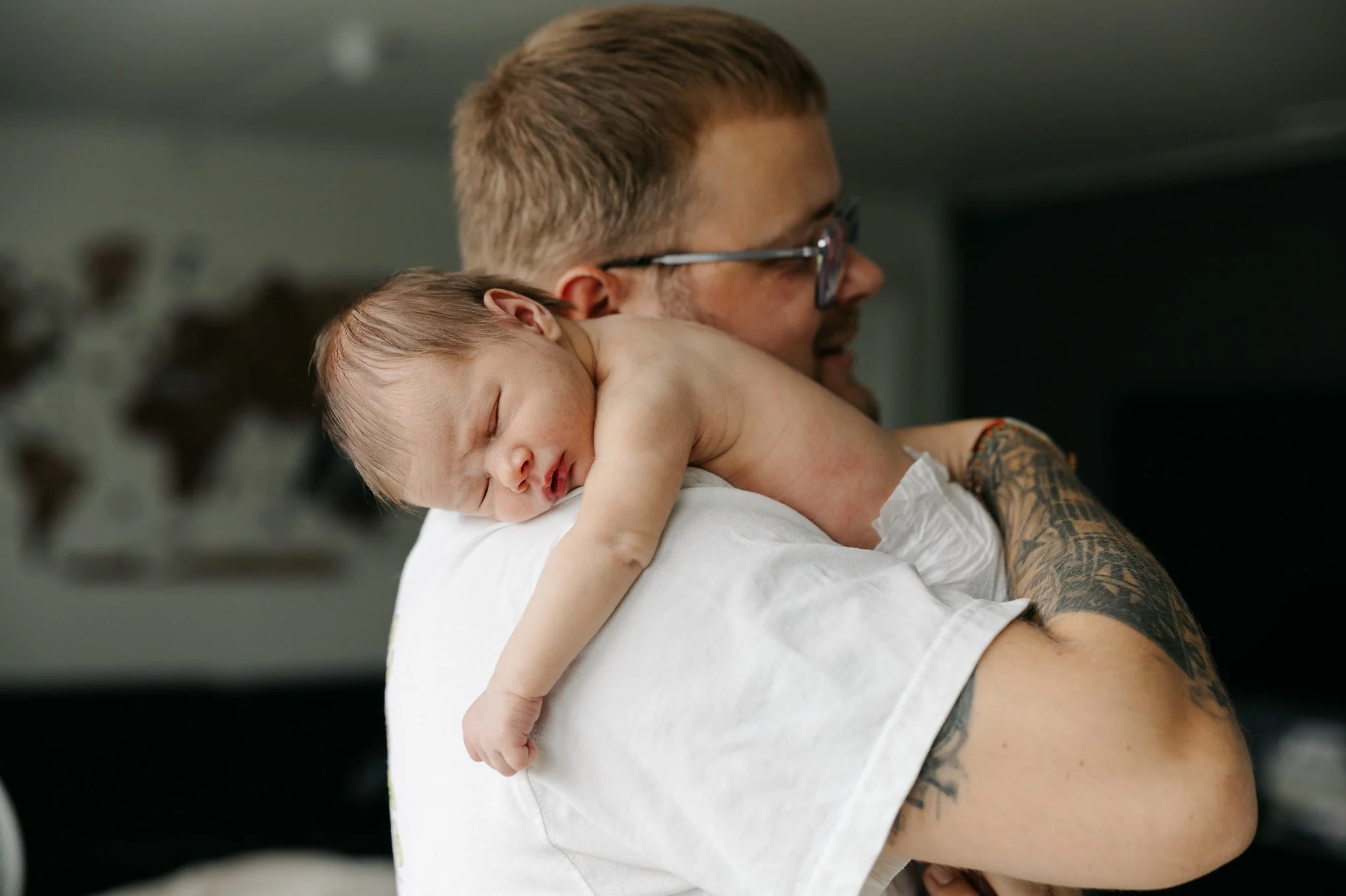 Far holder sin sovende nyfødte baby tæt ind til sig under en nyfødtfotografering.