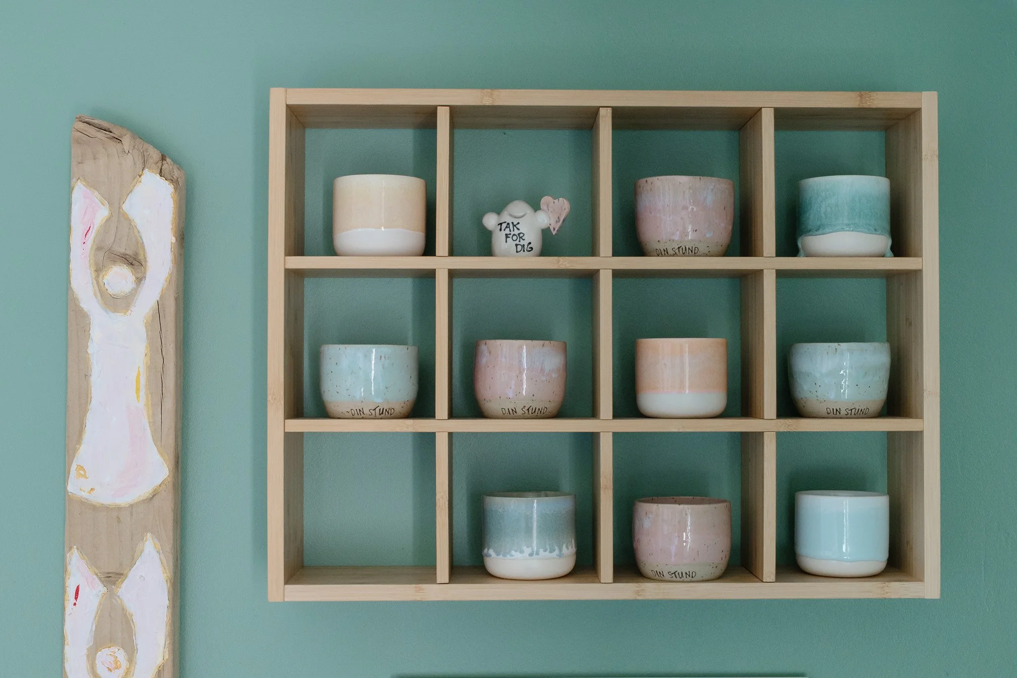 En træk shelves med ni forskellige sukkerkrukker på en lyst træhylde foran en turkis væg.