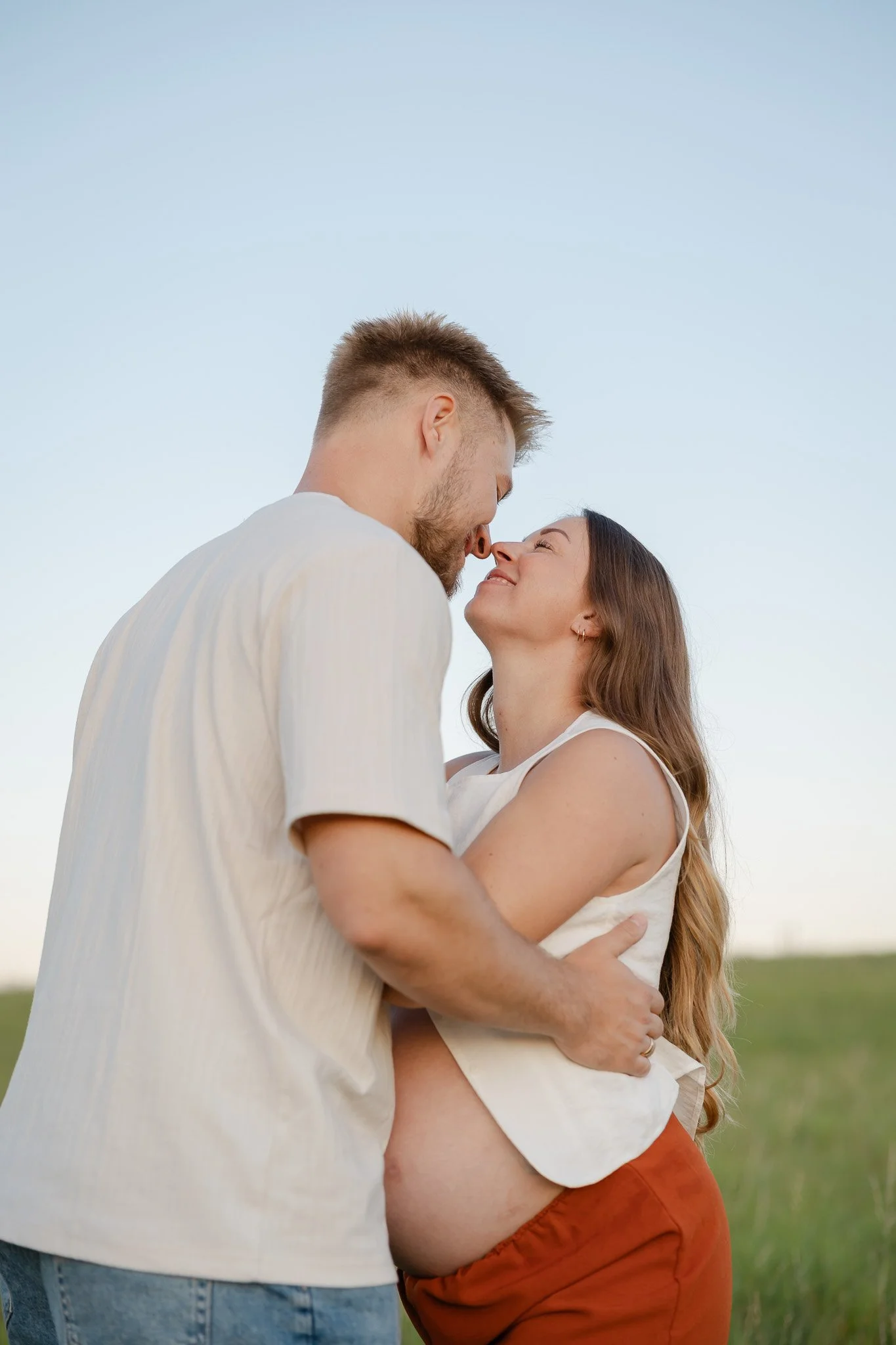 Gravid kvinde og hendes partner omfavner hinanden kærligt under en udendørs graviditetsfotografering.