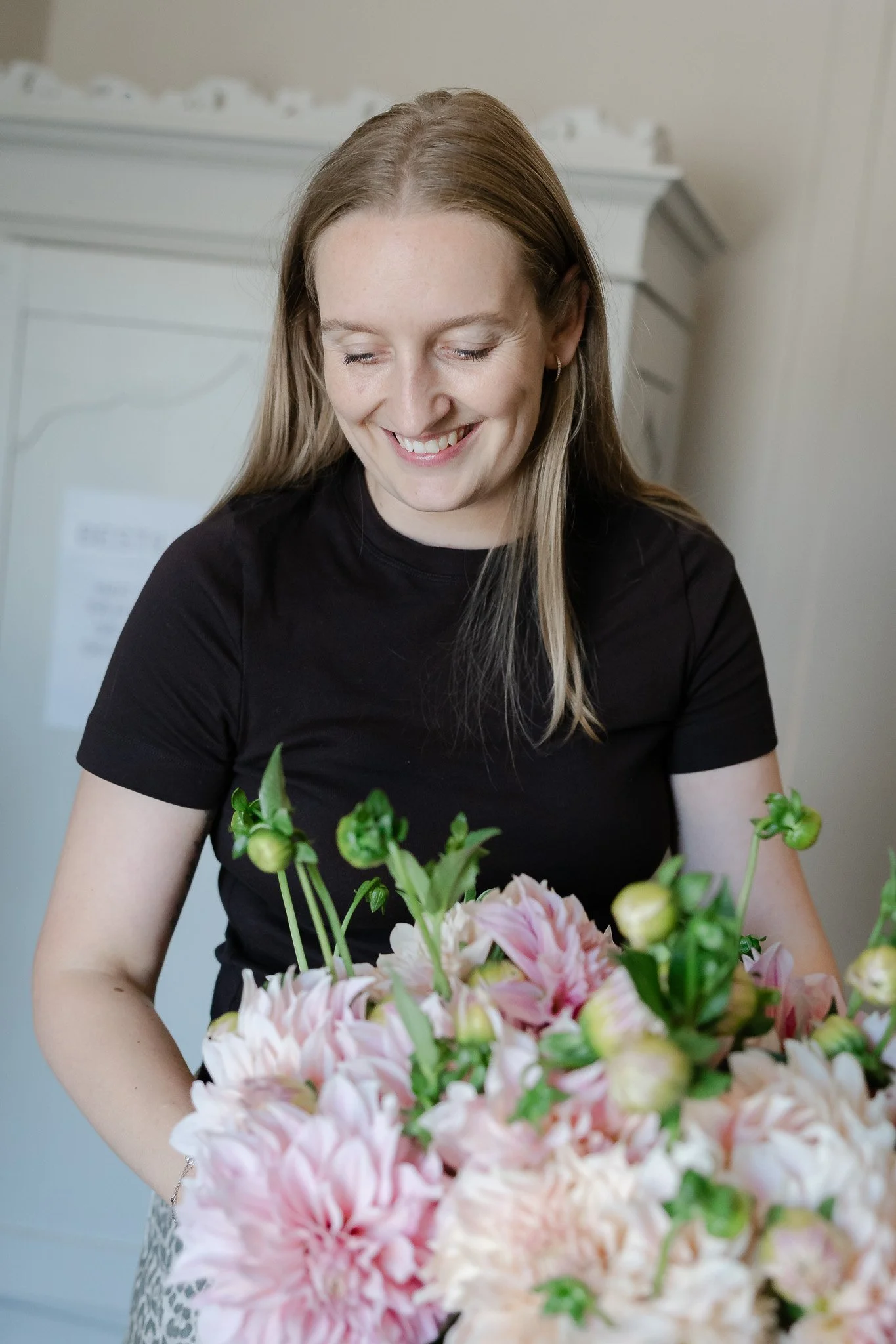 En smilende kvinde har en buket med lyserøde og hvide blomster.