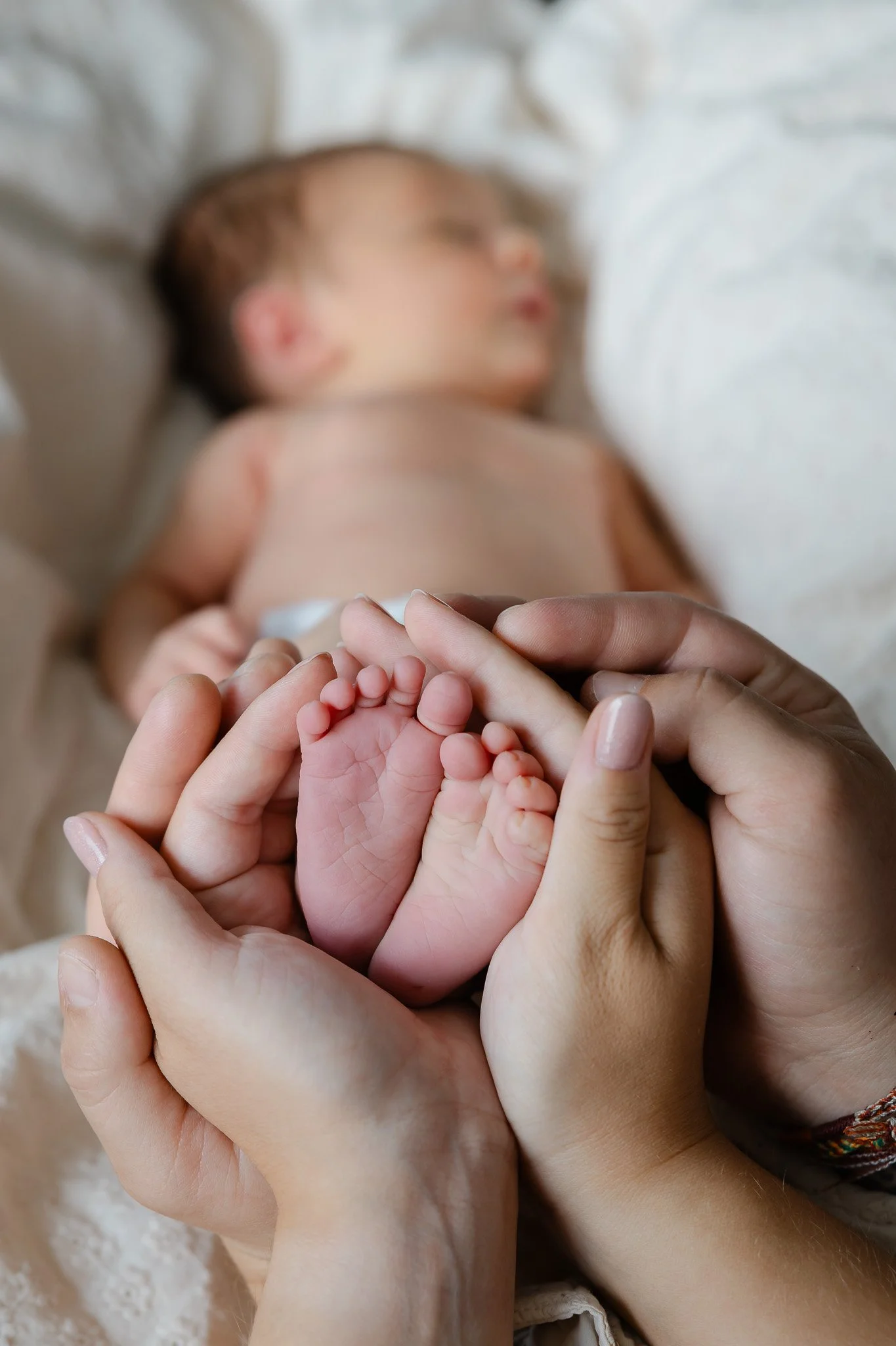 Nyfødt babys små fødder holdes forsigtigt i forældrenes hænder under nyfødtfotografering.