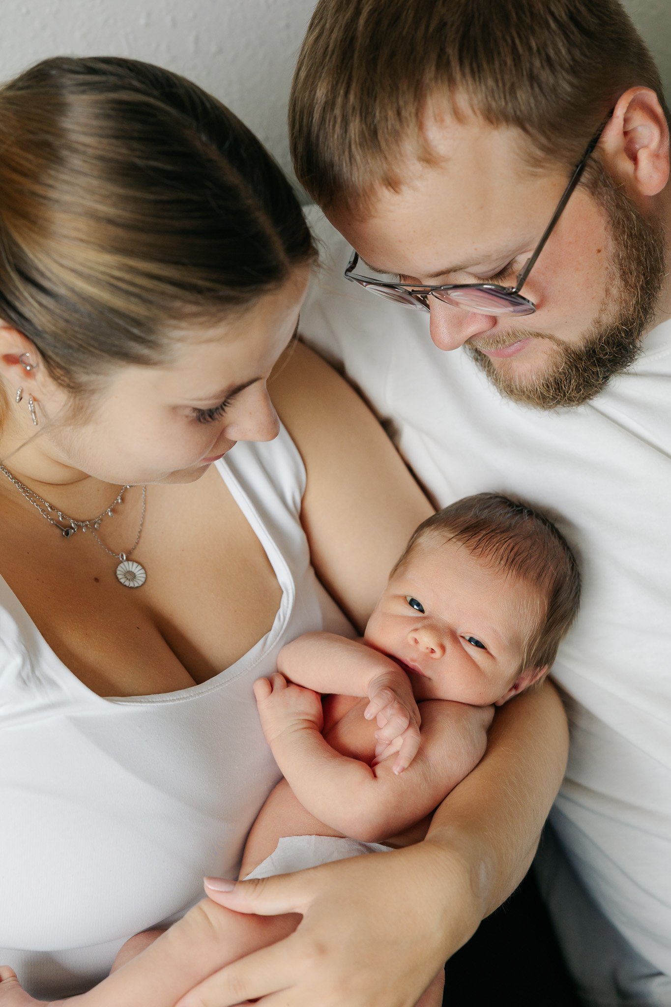 Nyfødtfotografering med baby i mors arme, mens begge forældre ser kærligt på barnet.