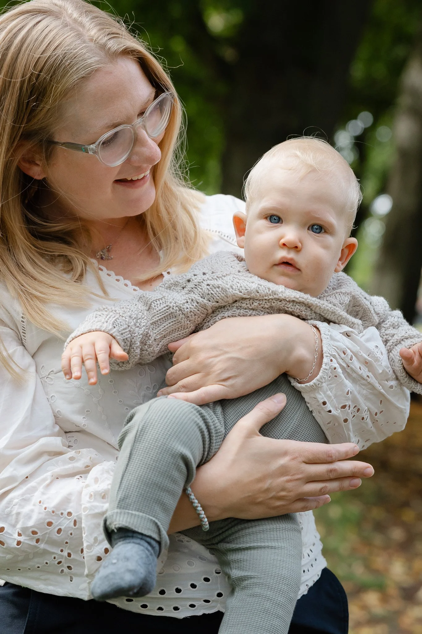 En mor holder sin lille 3-måneders dreng der kigger nysgerrigt ind i kameraet til familiefotografering udendørs i efteråret