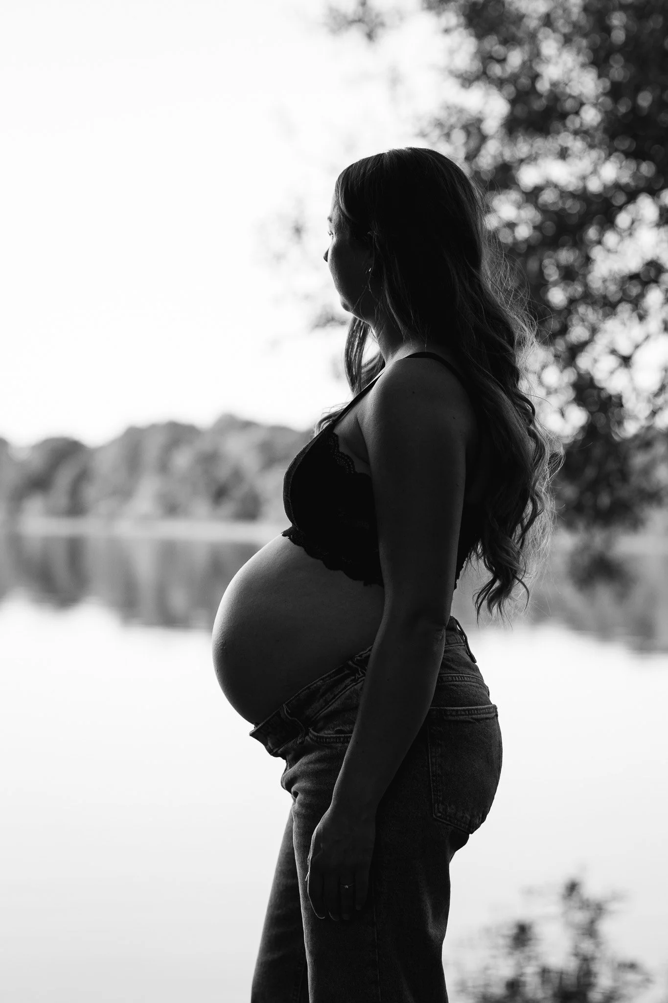 Sort-hvid silhuet af en gravid kvinde med langt hår, fotograferet ved vandet.
