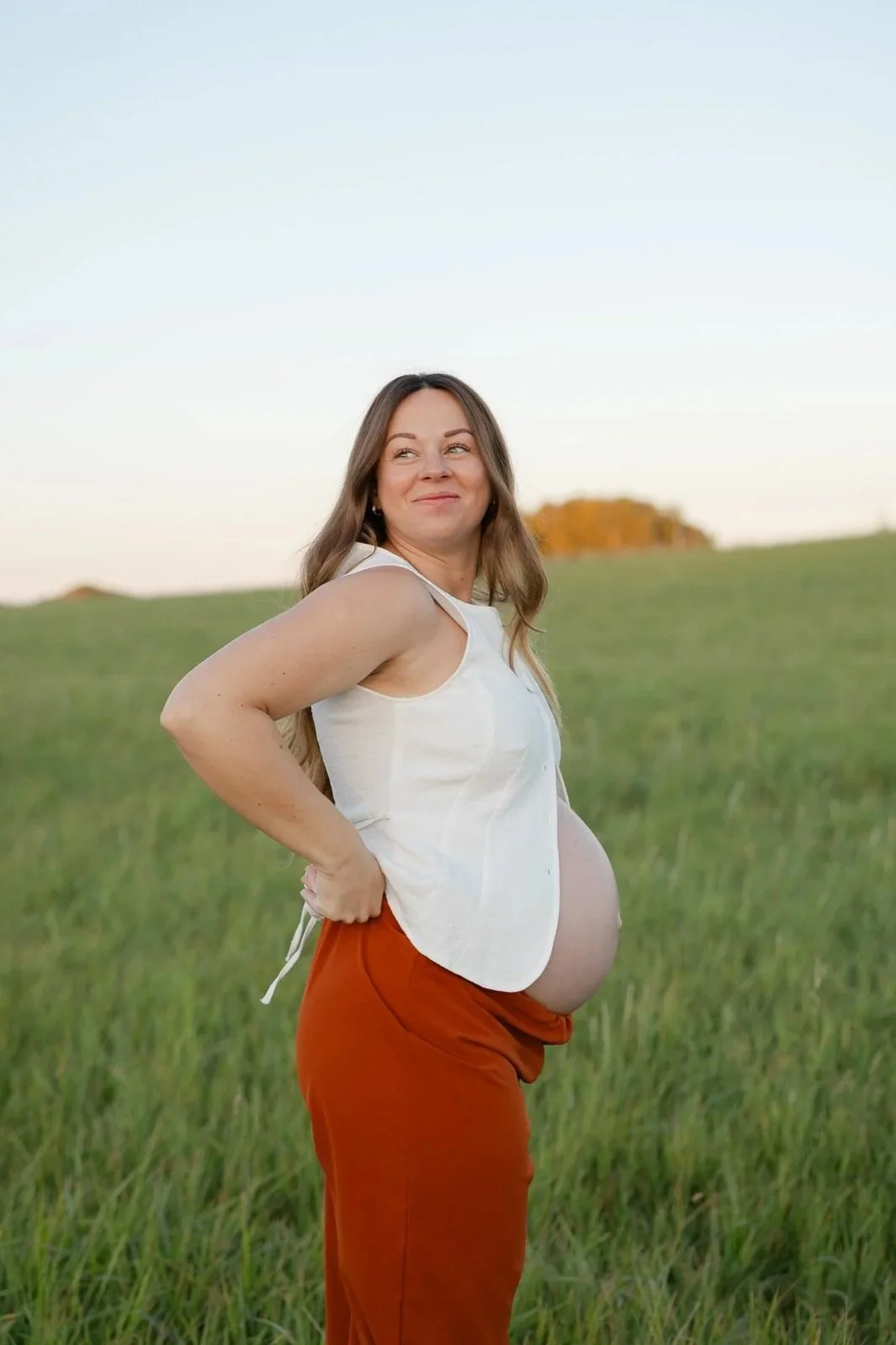 Graviditetsfotografering af en kommende mor i en grøn eng i det bløde aftenslys.