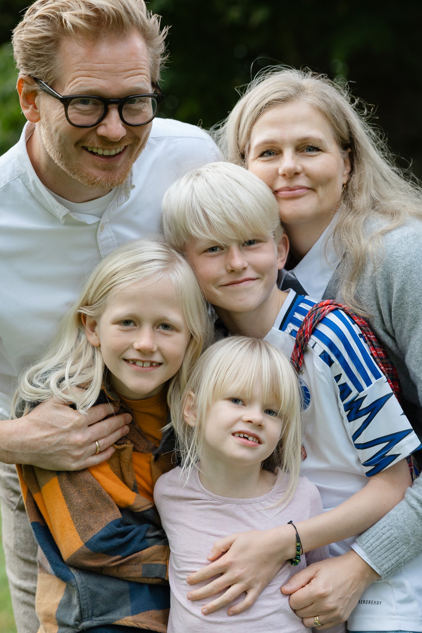 En lyshåret familie på 5 med far mor, 2 storebrødre og en lillesøster står og holder om hinanden og ser glade ud til familiefotografering udendørs i efteråret